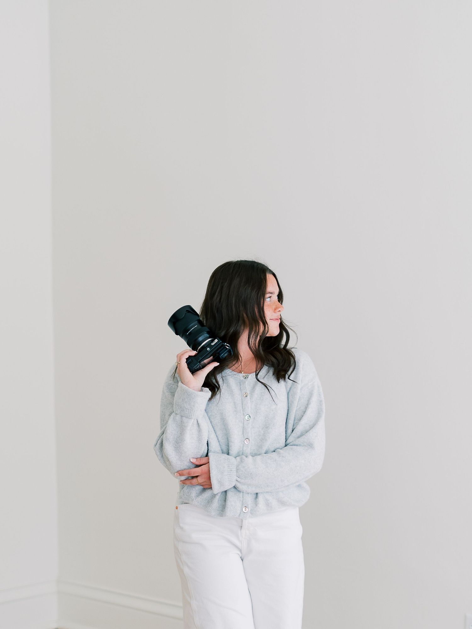 Person in white outfit poses against light wall while holding professional camera in multiple artistic shots.