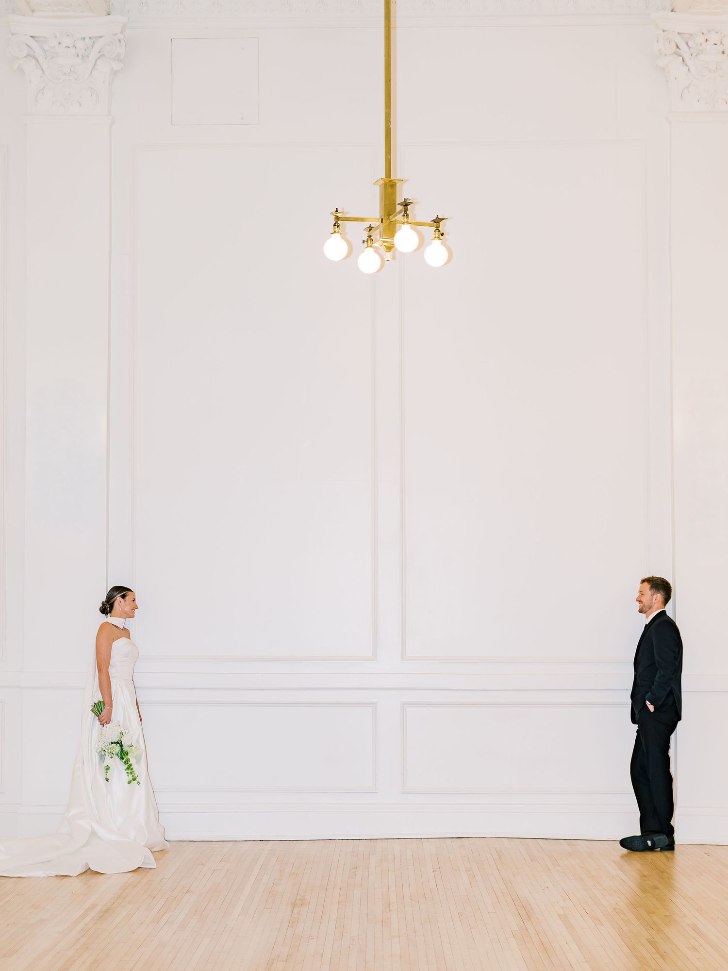 A minimalist wedding photoshoot sequence showing a couple in a white room with elegant moldings and a brass chandelier.