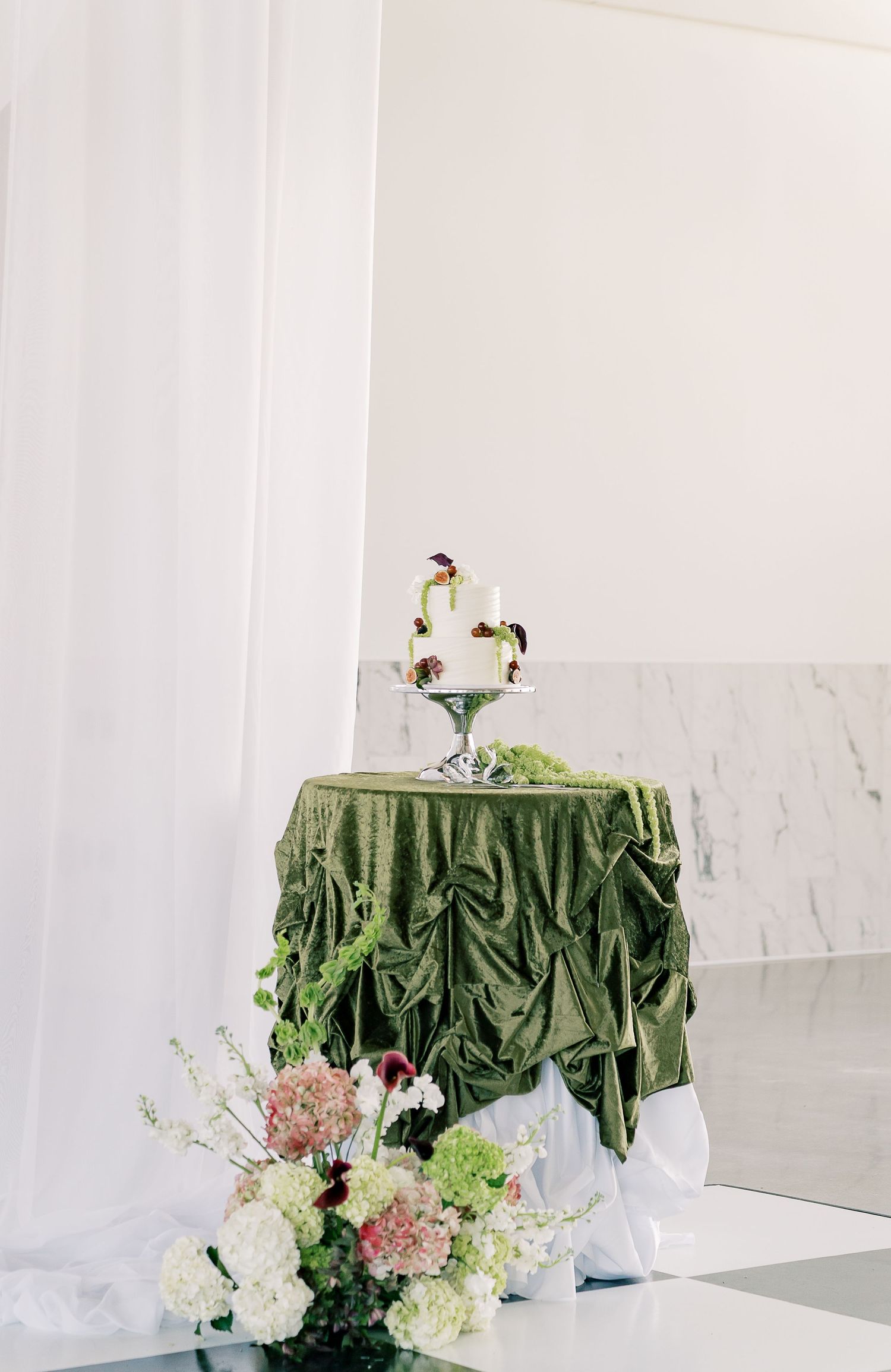 Round cocktail tables with elegant green velvet tablecloths and floral centerpieces in white and blush tones at an event.