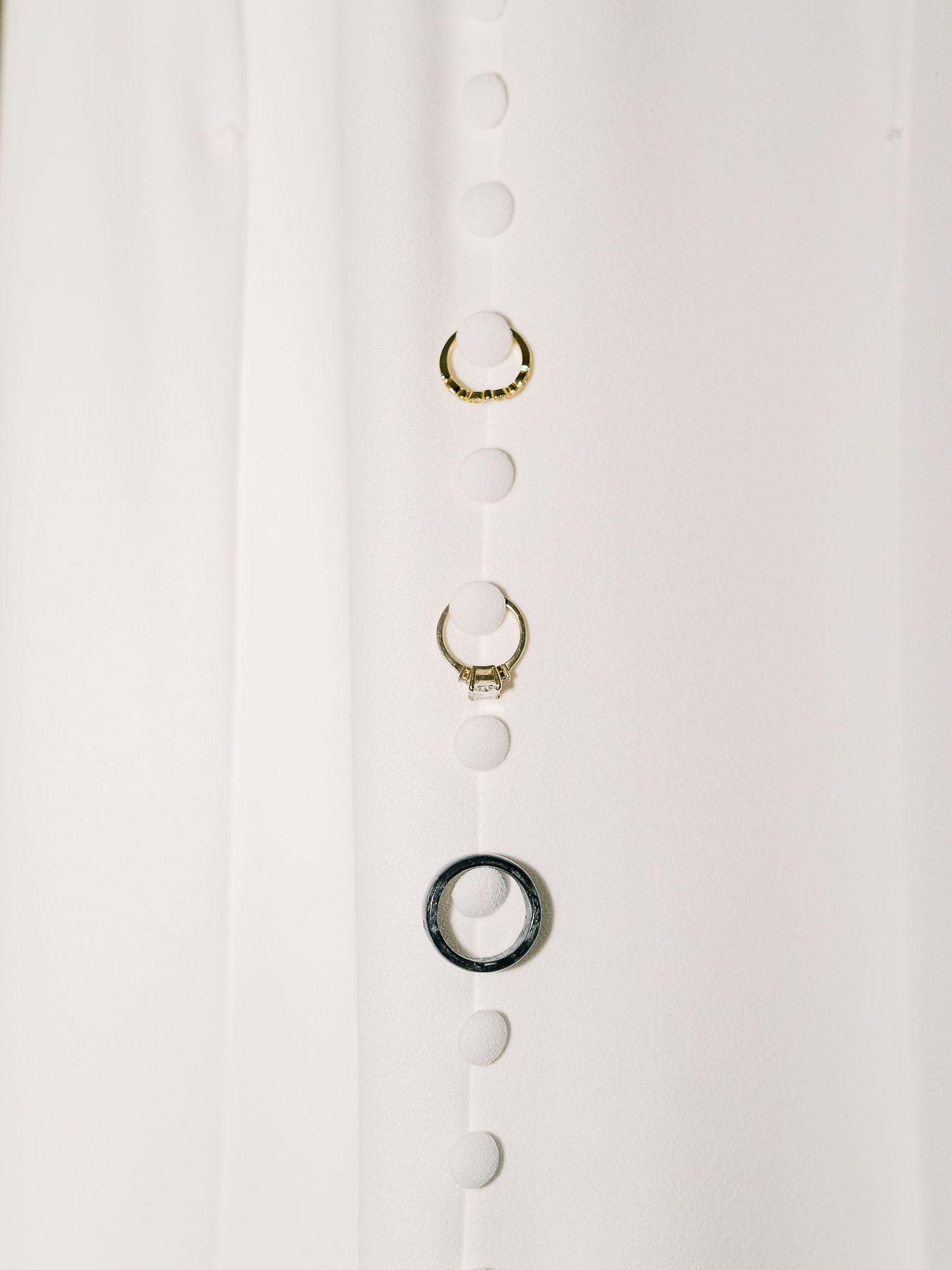 Three delicate rings arranged vertically on a white surface, featuring two gold bands and one silver ring with minimalist designs.