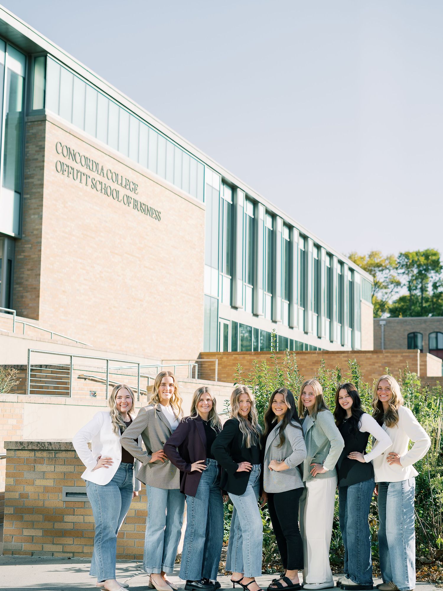 A group of students in casual attire pose together against a brick building exterior in a playful lineup.