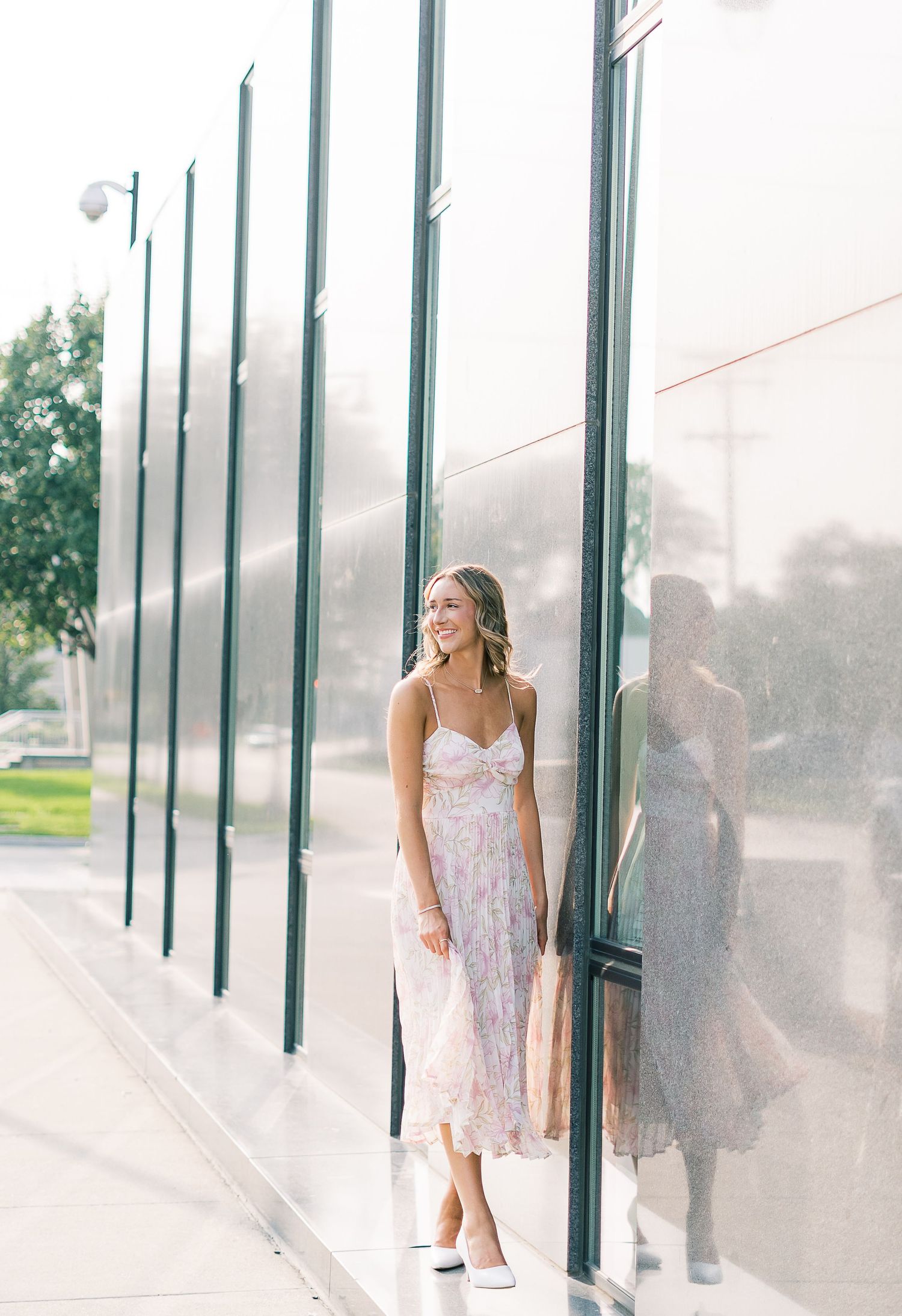 A series of five connected images showing someone in a floral dress posing against a glass wall in natural light.