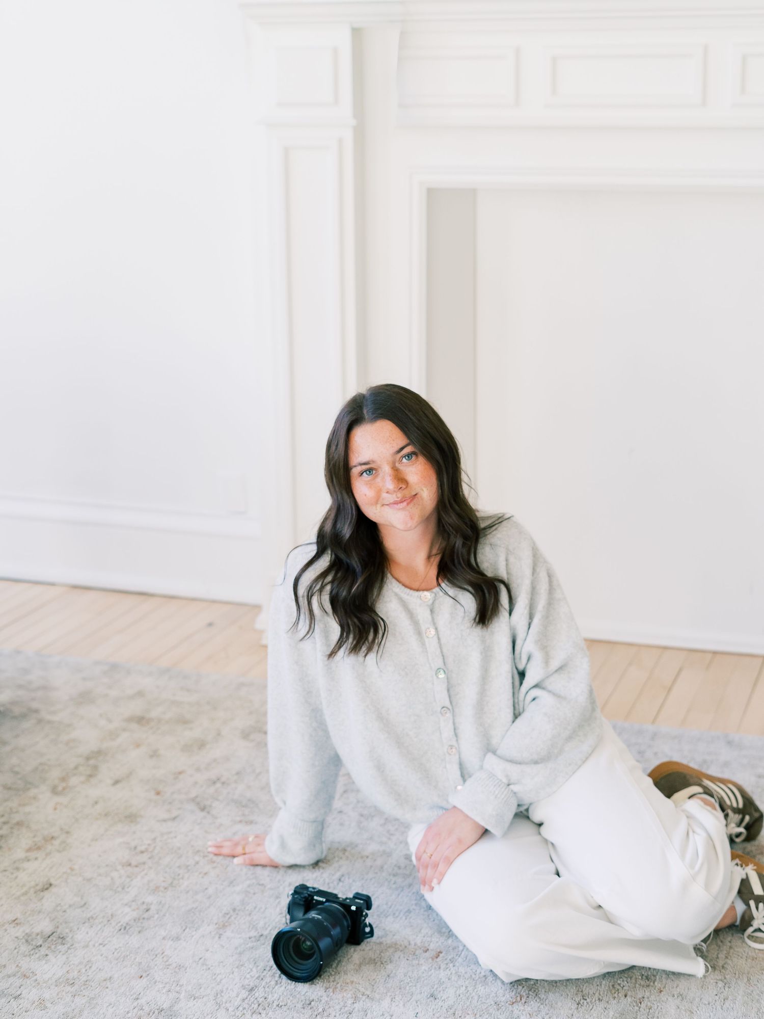 A person in a cozy cream-colored sweater relaxes on a light carpet in a bright, minimalist interior setting.