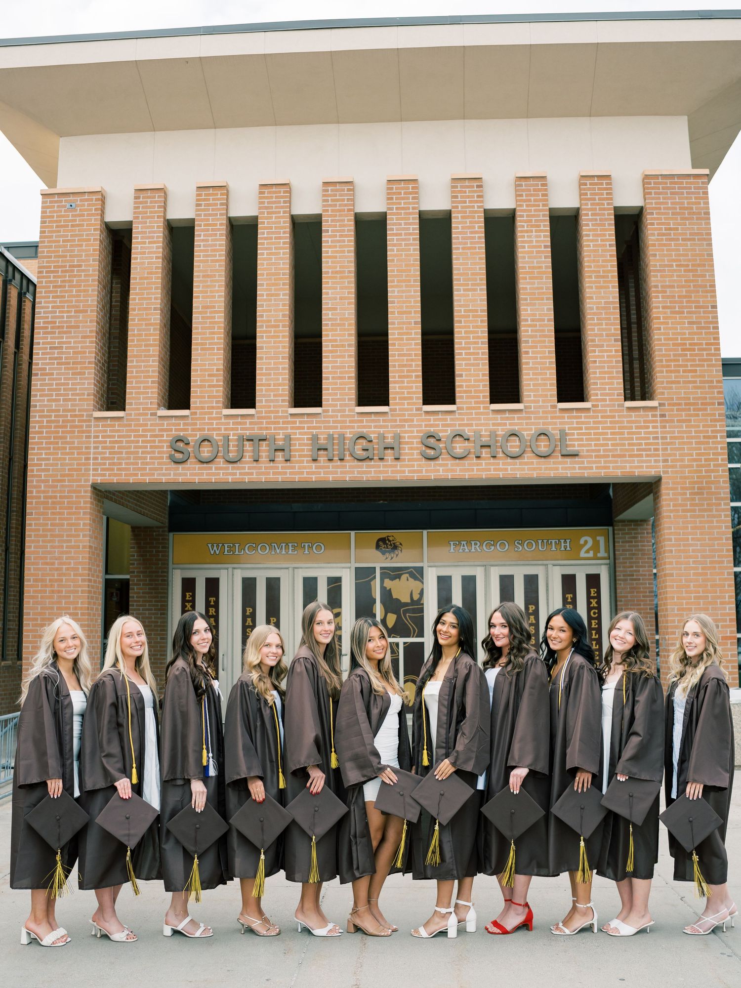 Group of female high school graduates in caps and gowns posing in front of South High School building.