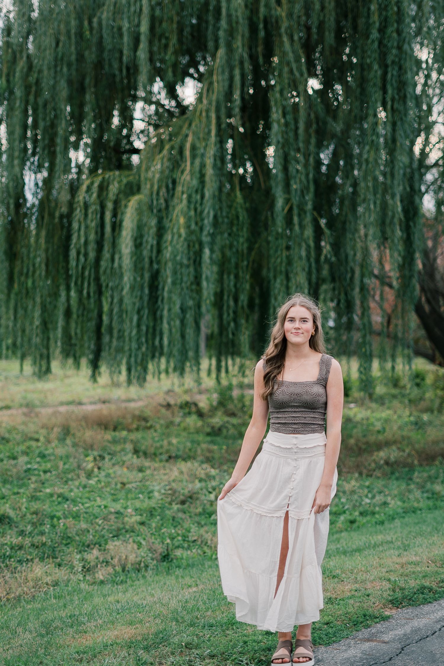 A series of outdoor portraits showing a person in a brown and white dress posing under weeping willow trees.