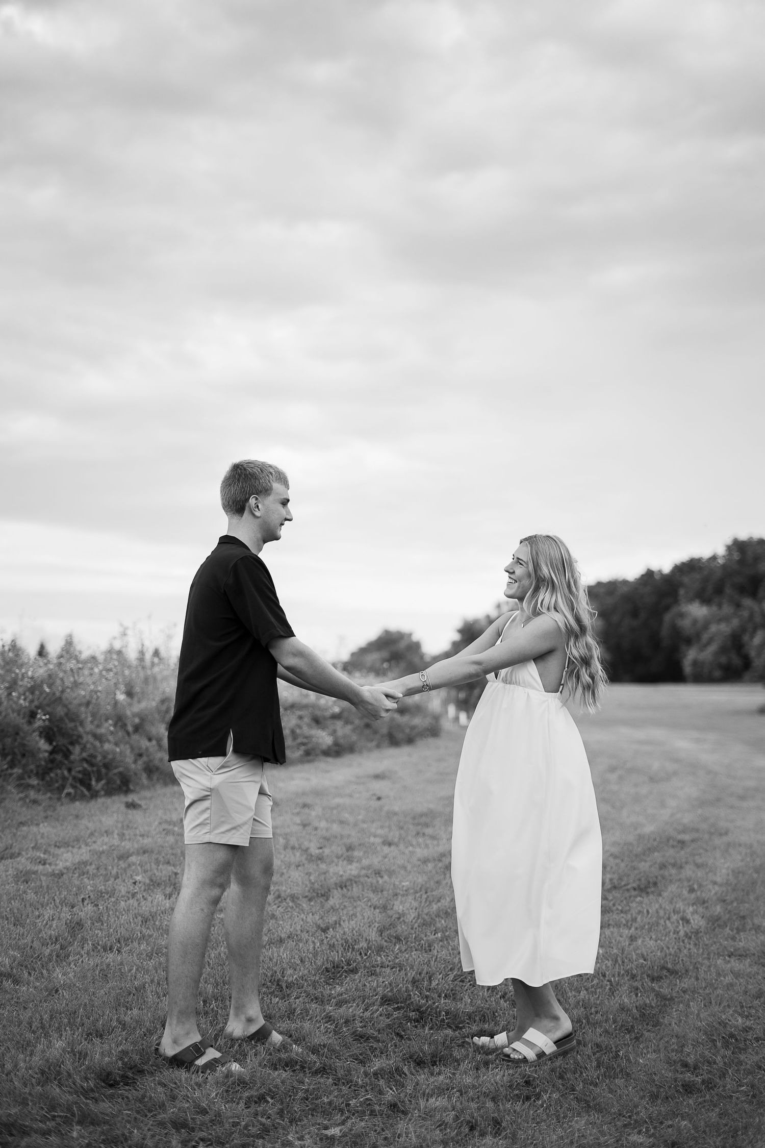 Black and white sequence of a couple playfully walking and twirling together in a grassy meadow field.