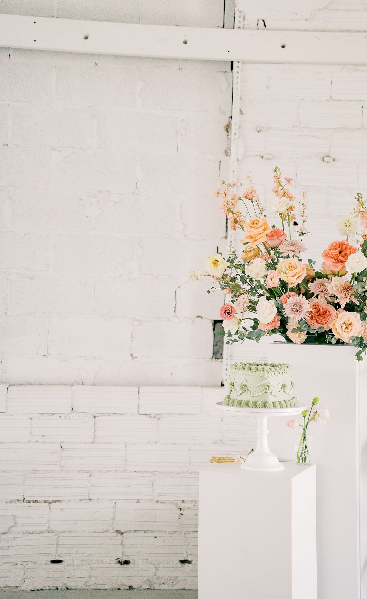 Peach and coral flower arrangements adorn white shelves against a rustic white brick wall in a minimalist setting.