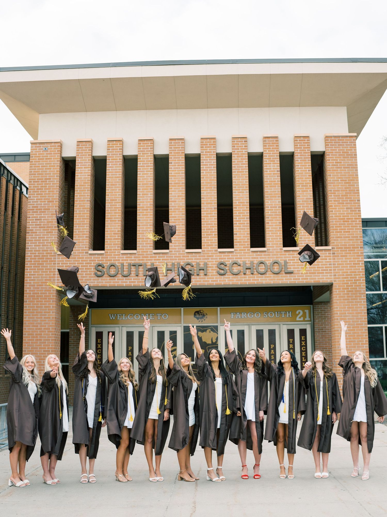 Female graduates in black gowns toss caps in front of South High School building in a celebratory group photo.