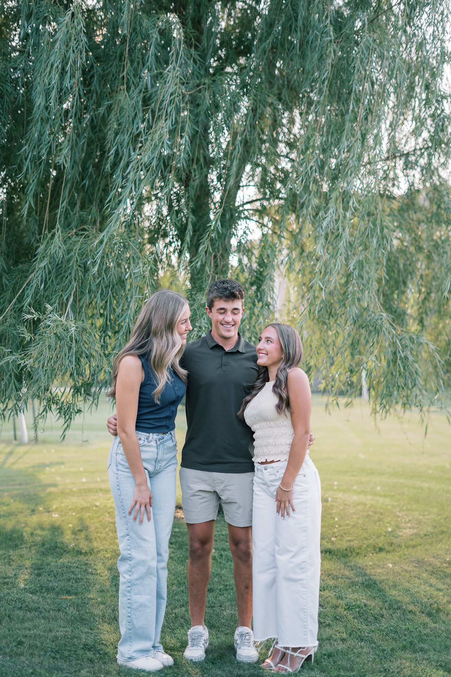 Family shares candid moments together under graceful weeping willow trees on a sunny afternoon in the park.