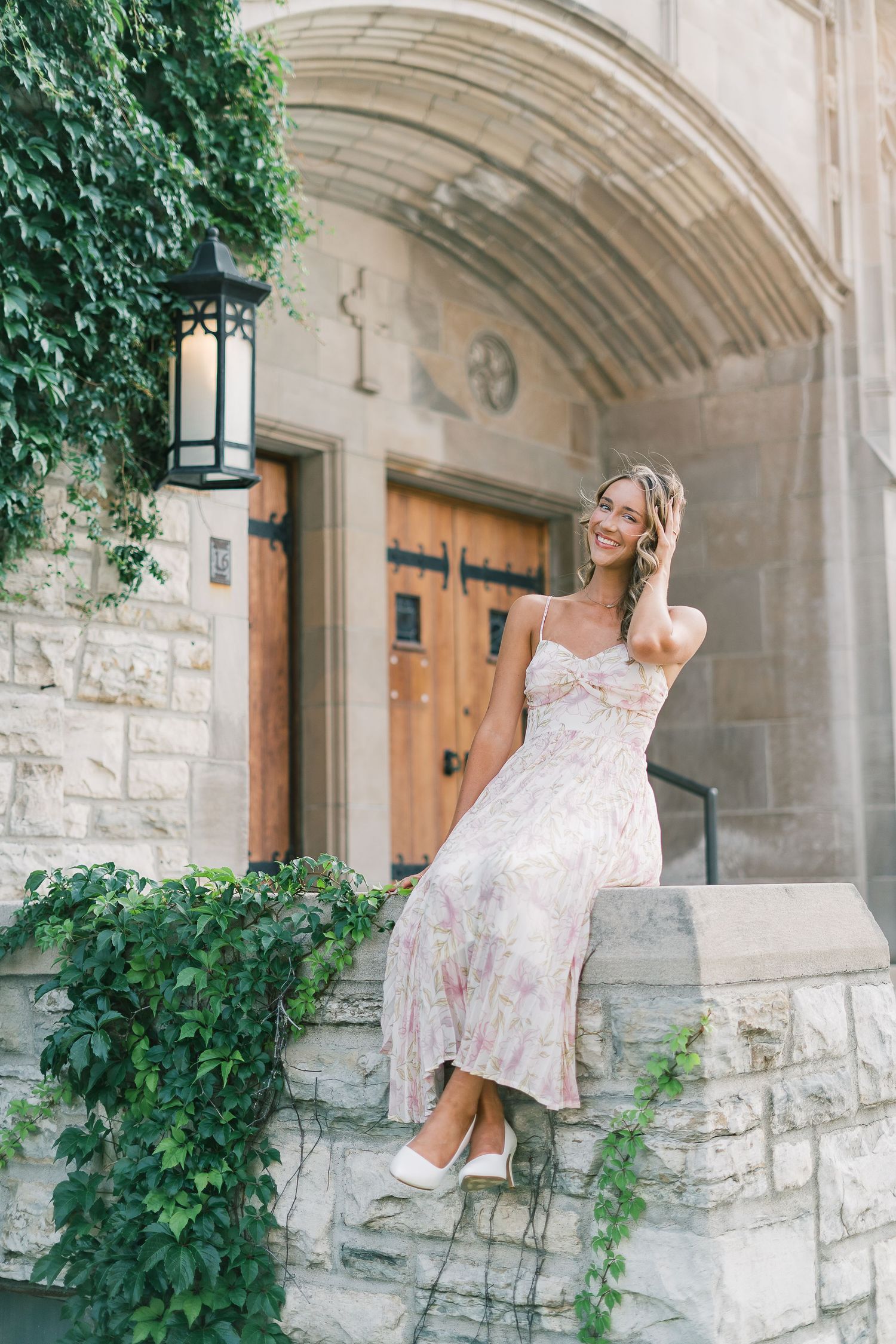 A floral sundress and white heels complement the elegant stone archway and historic wooden door of a church entrance.