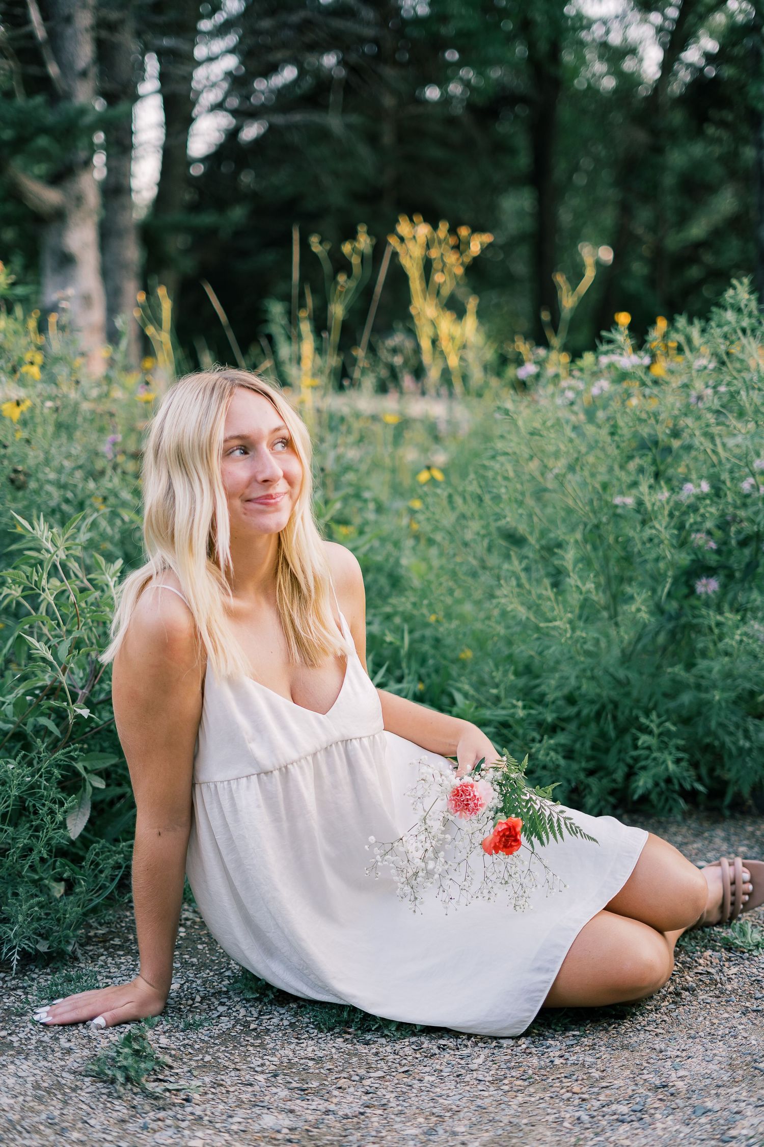 A person in a white summer dress reclines on a garden path surrounded by yellow wildflowers and greenery.