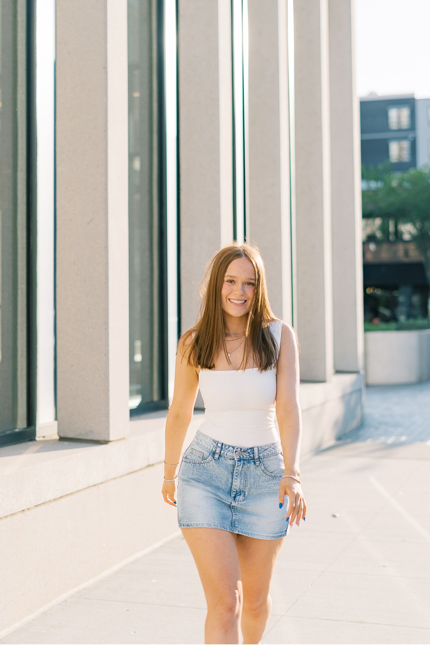 A person wearing denim shorts poses against a modern white colonnade with clean architectural lines.
