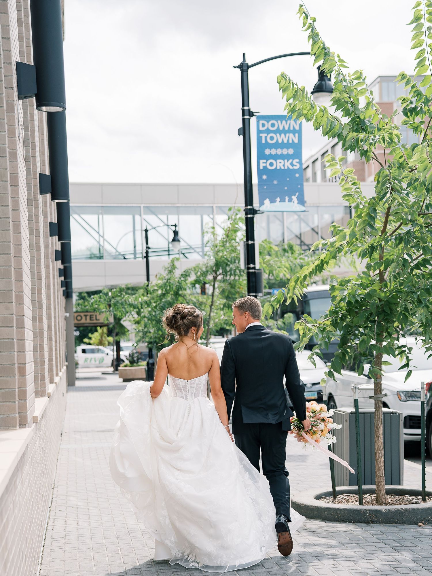 A couple walks together along a covered outdoor walkway with trees and lamp posts on a cloudy day.