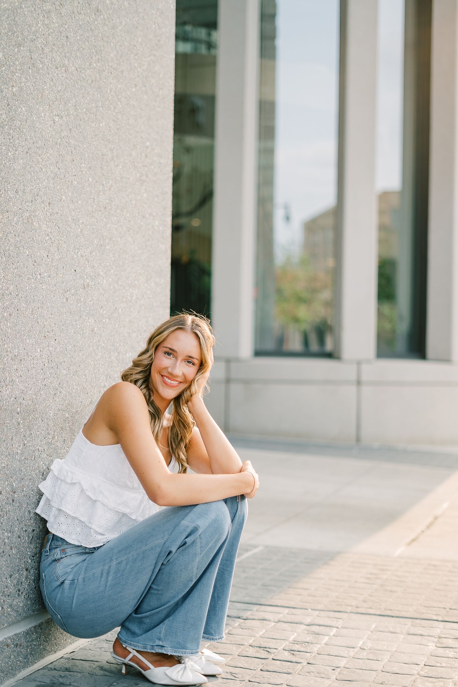 Person in white top and jeans poses casually against architectural columns in outdoor portrait series.