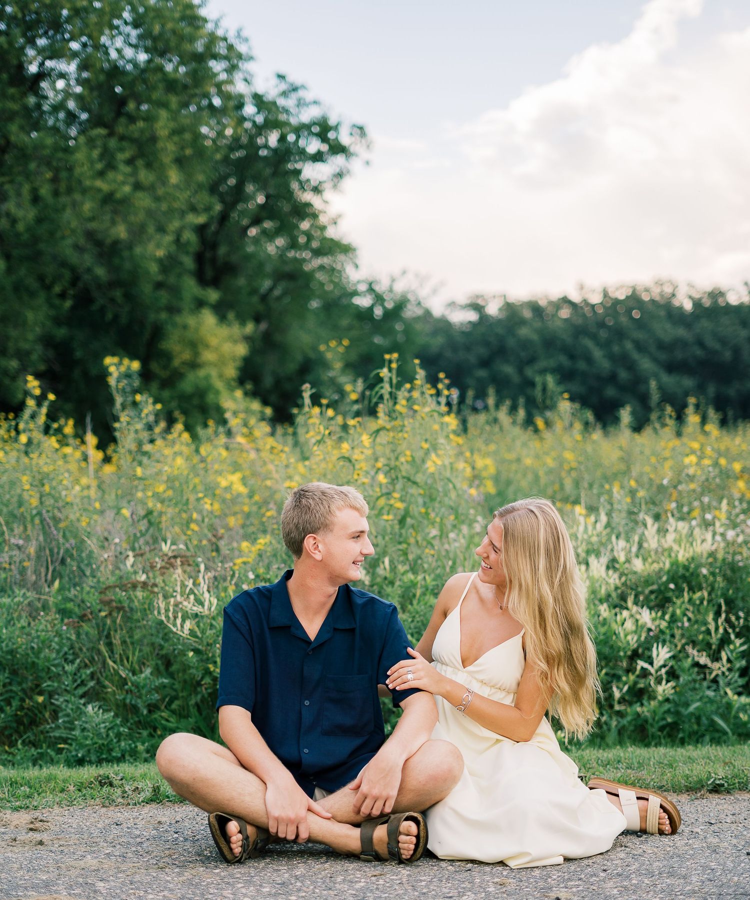 A romantic couple lounges together in a field of yellow wildflowers on a summer afternoon.