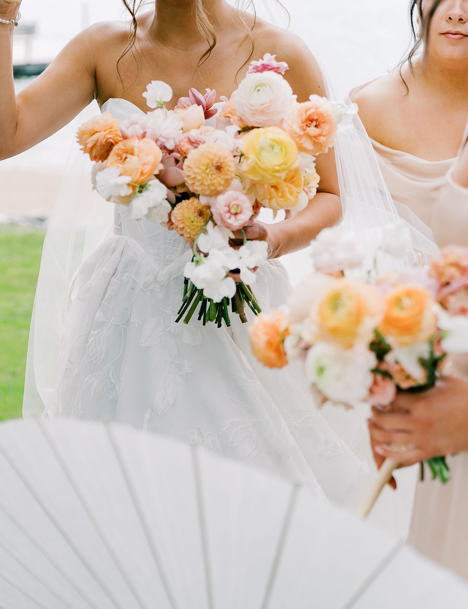 Beautiful peach and blush wedding bouquets with garden roses and peonies held against white wedding dresses.