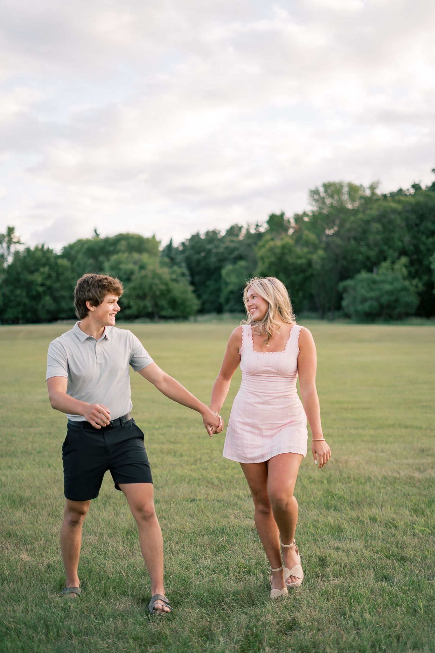 Couple playfully dancing together in a green field on a cloudy summer day.