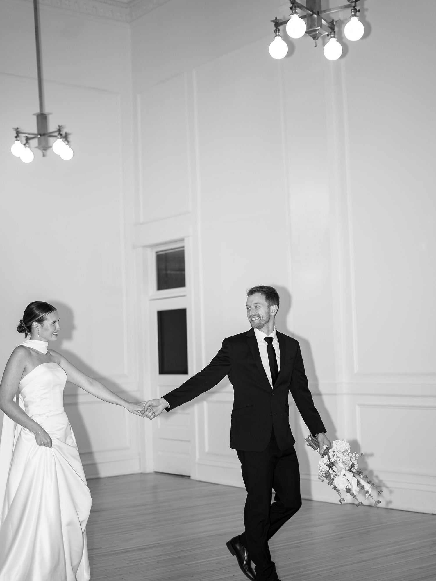 A black and white photo series shows a playful wedding couple dancing and posing in an elegant white room.