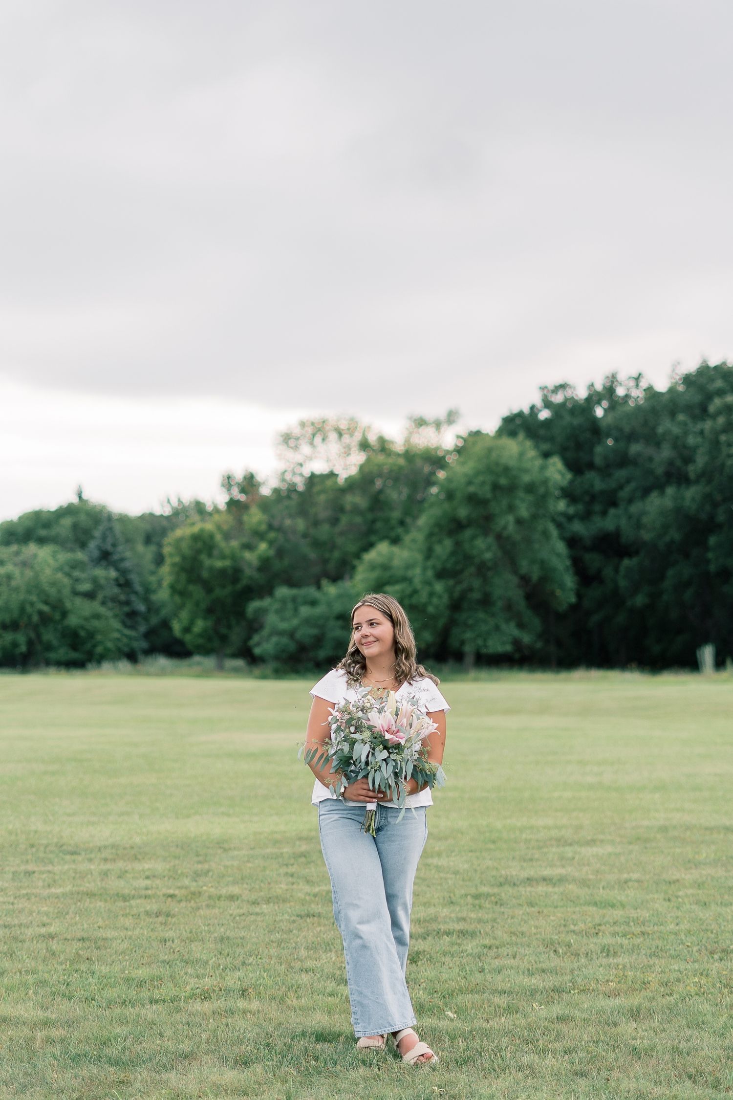 A person in light denim jeans and white top gathers wildflowers in a lush green meadow on a summer afternoon.