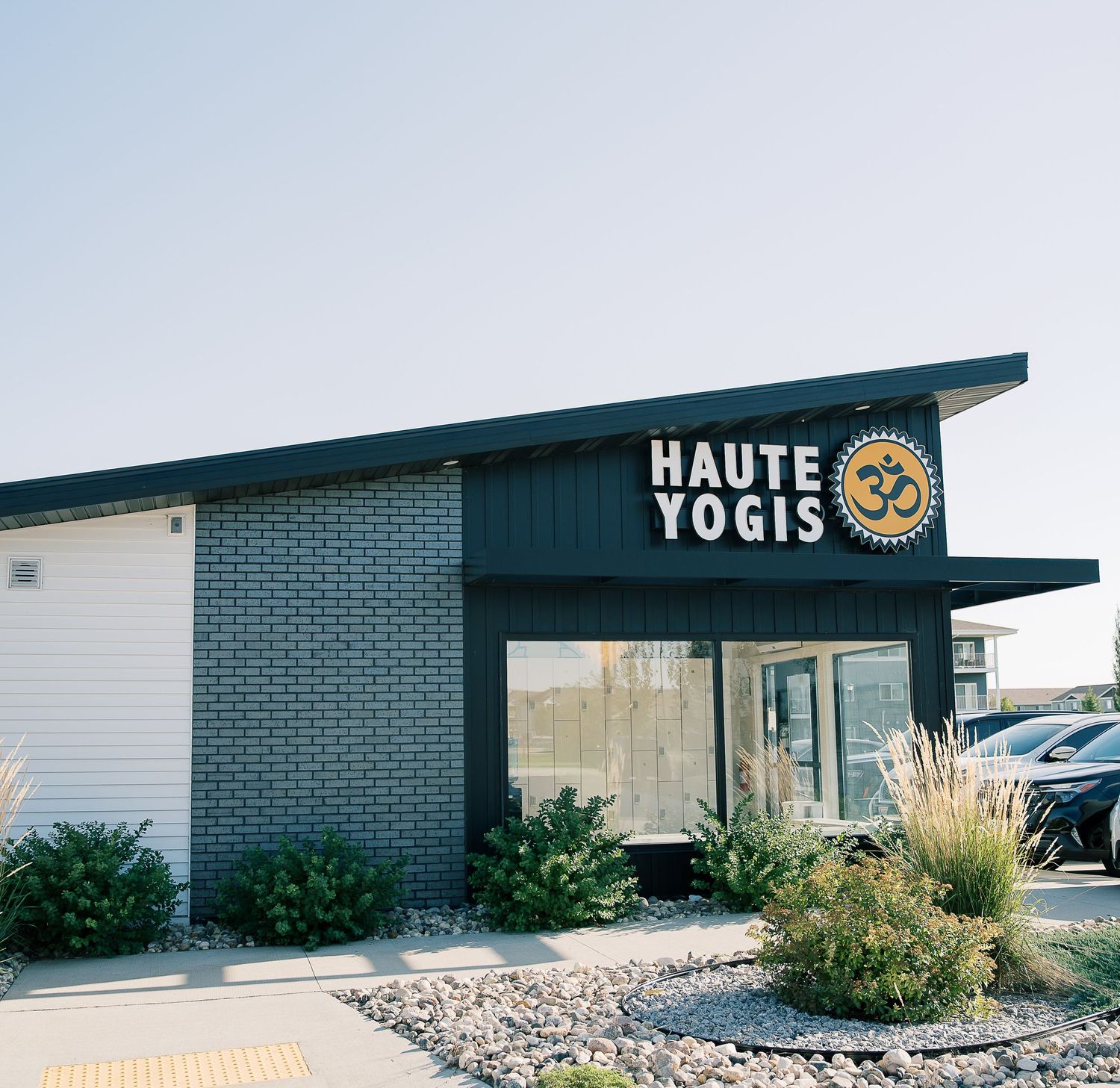 Modern brick building with Haute Yogis yoga studio signage and decorative landscaping featuring ornamental grasses.