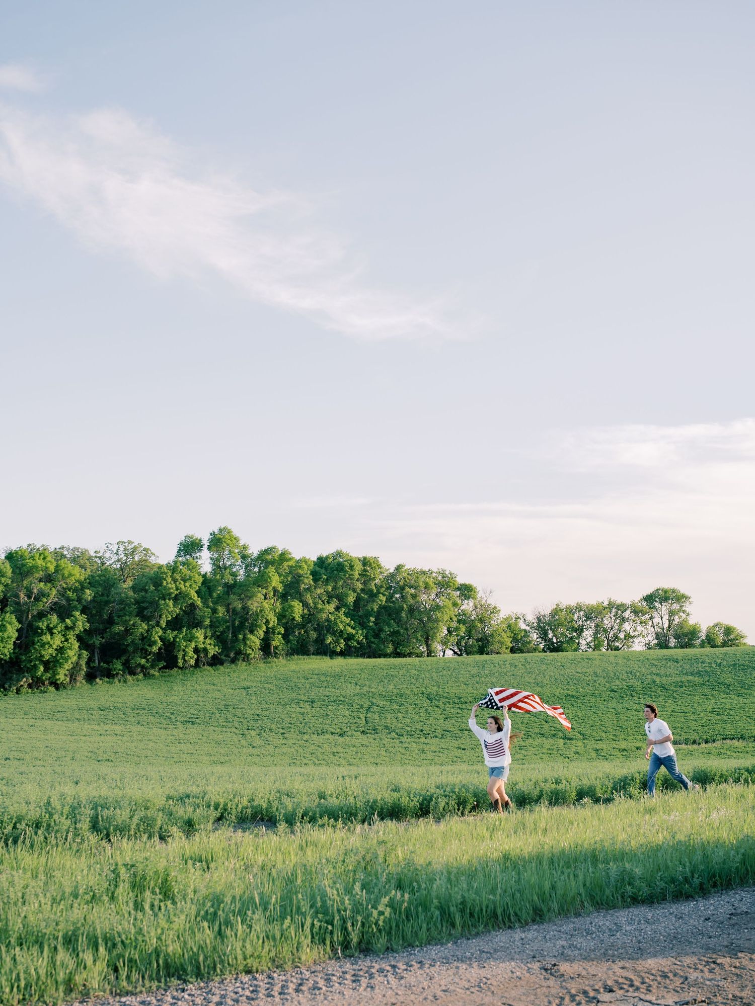 Two people running through a green field waving an American flag on a sunny day.