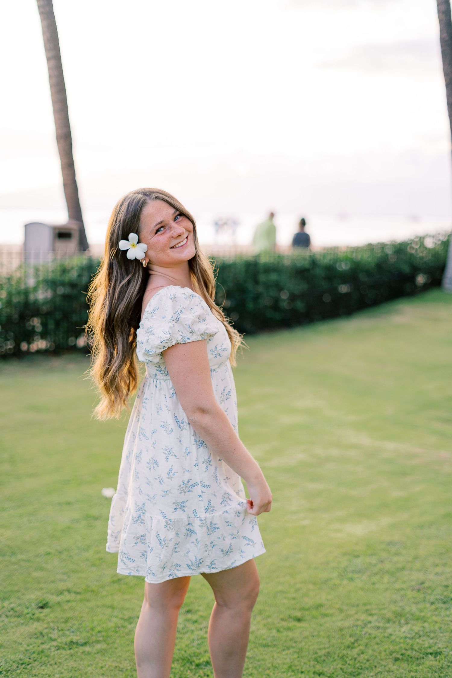 Someone in floral dress twirling on green lawn during sunny day.