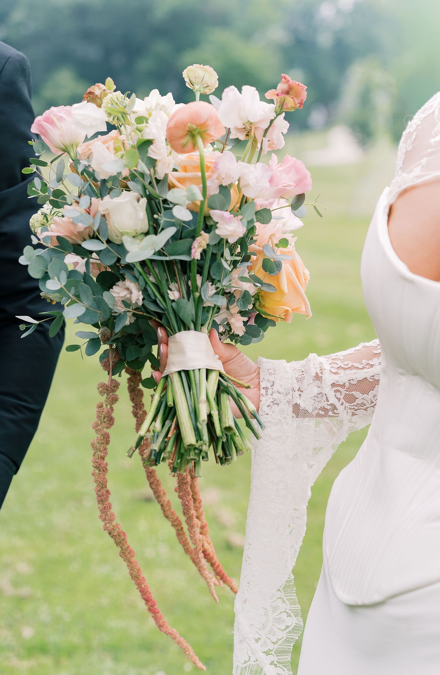 Beautiful wedding bouquet with pink and peach roses mixed with eucalyptus greenery held against a white lace dress.