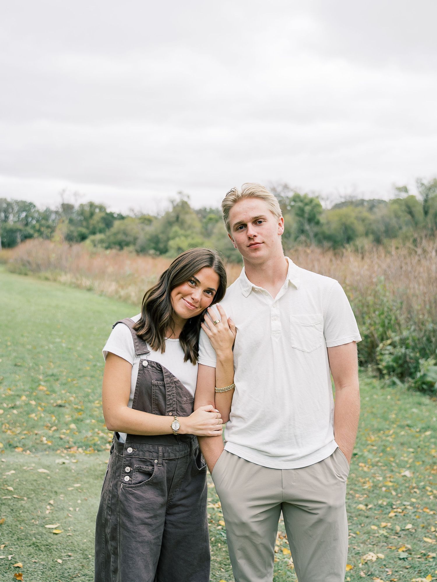 A couple poses together in a sunny field with wildflowers, wearing coordinating white and gray outfits.