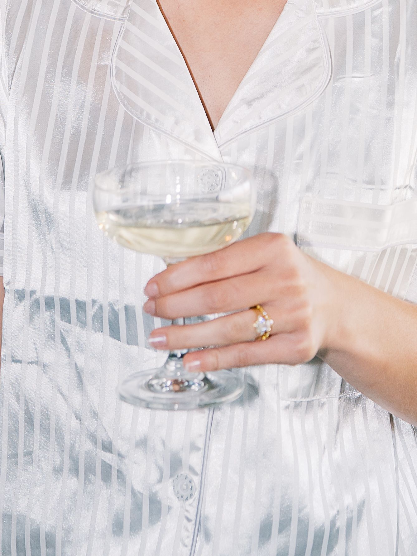 Hand in a white striped shirt holds a wine glass against a light background with soft shadows.