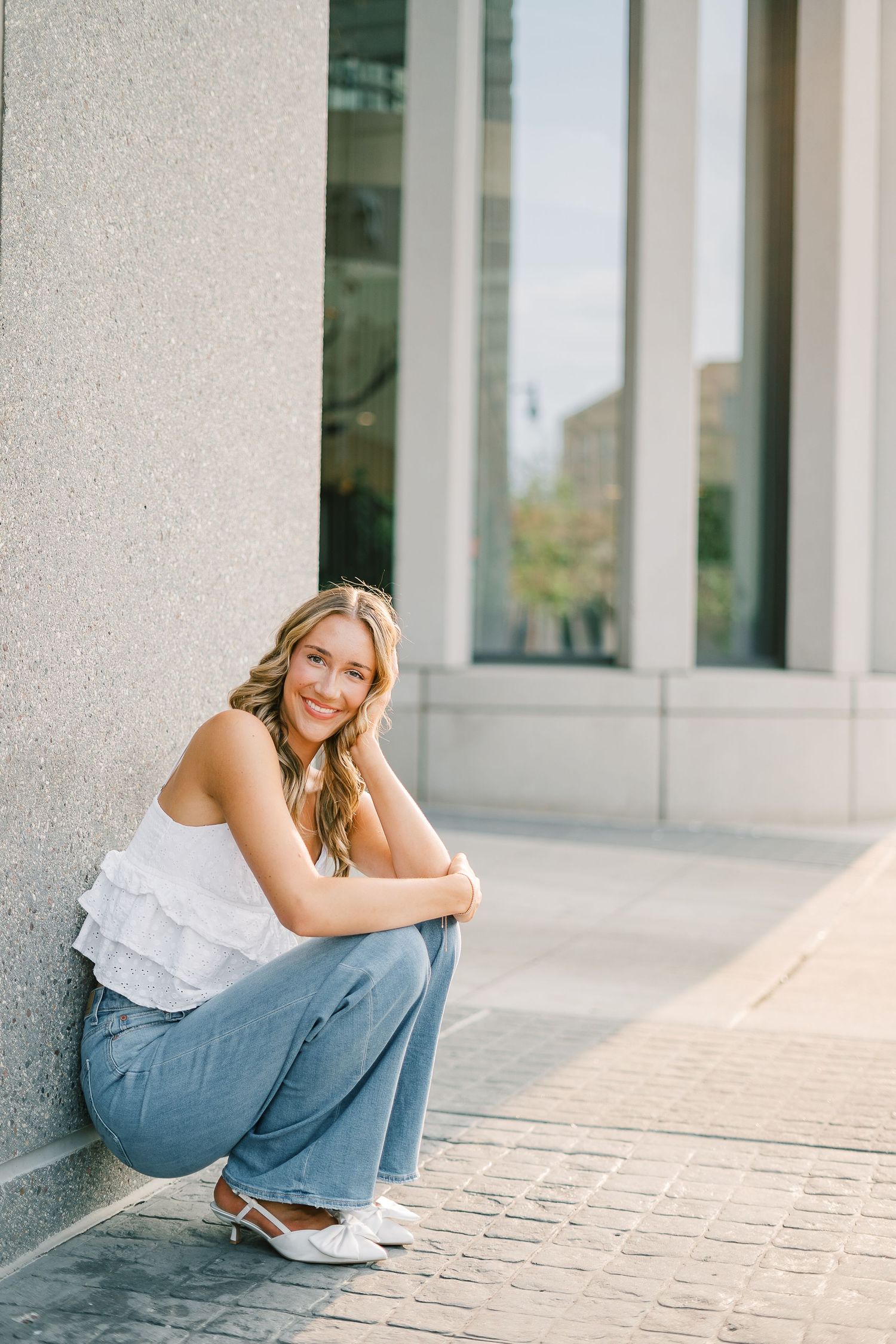 A casual portrait session featuring someone in jeans and white top sitting on stone steps in natural lighting.