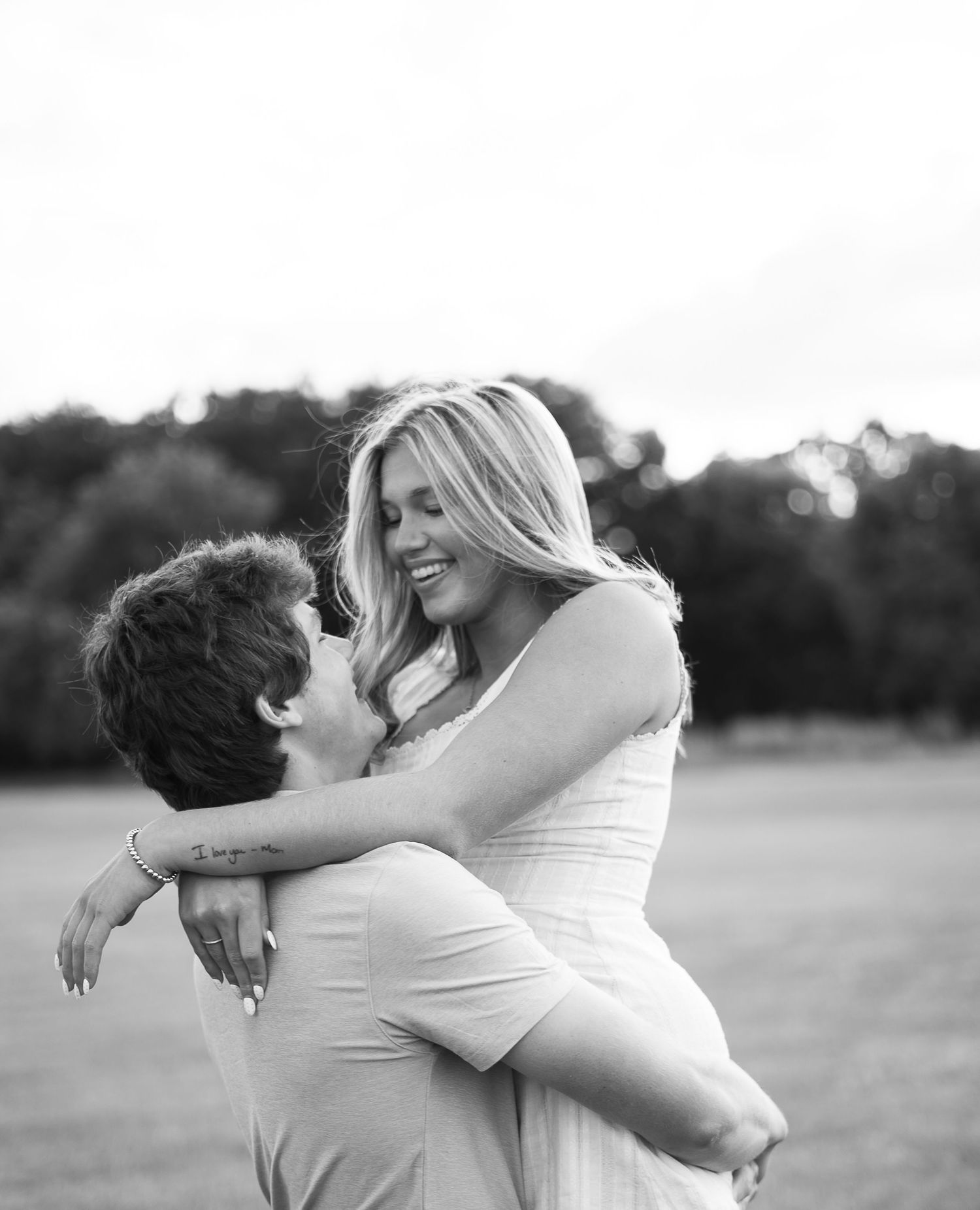 A romantic black and white portrait shows a joyful couple embracing in an outdoor field.