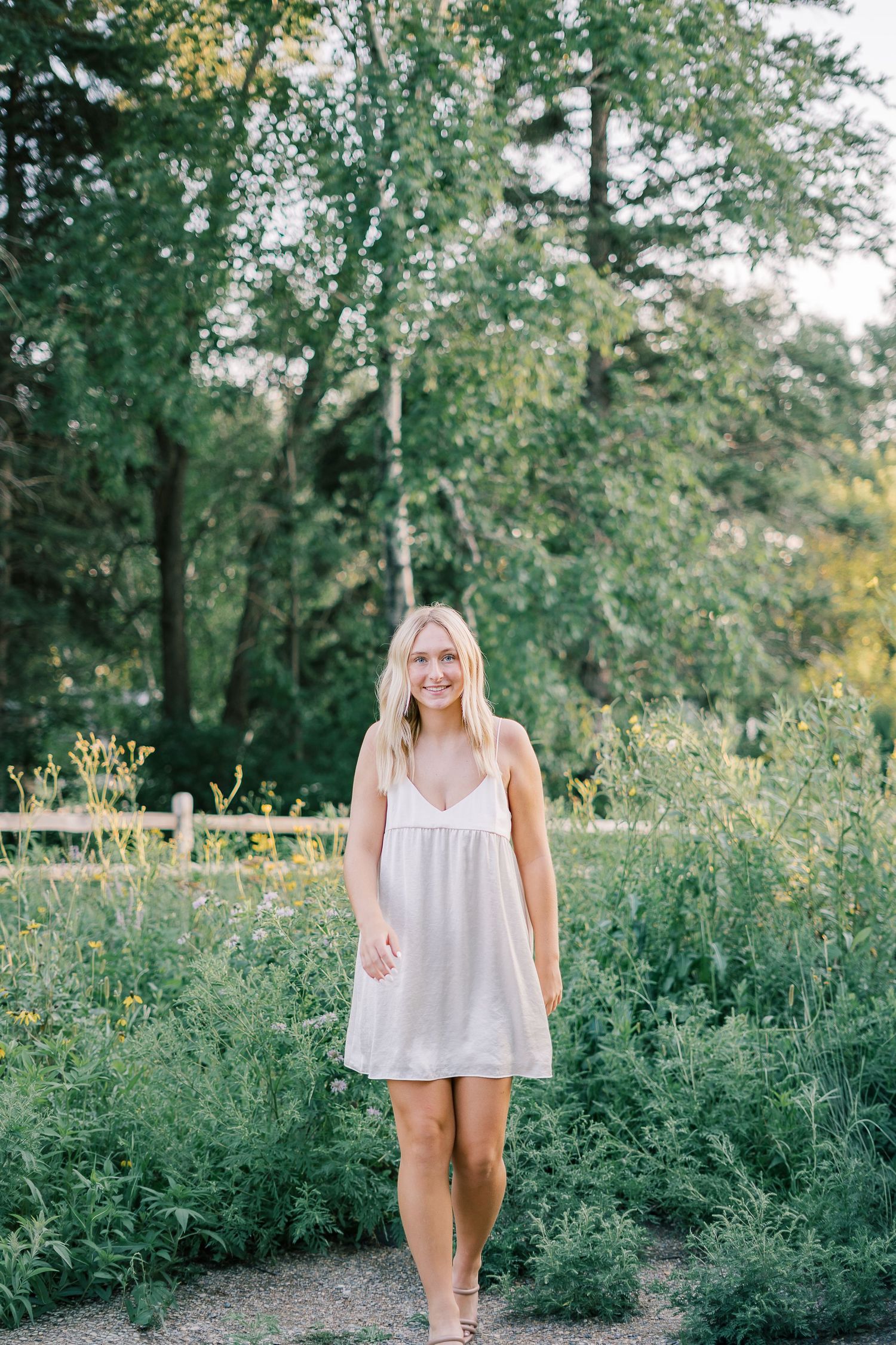 A white summer dress stands out against lush green foliage on a nature path during golden hour.