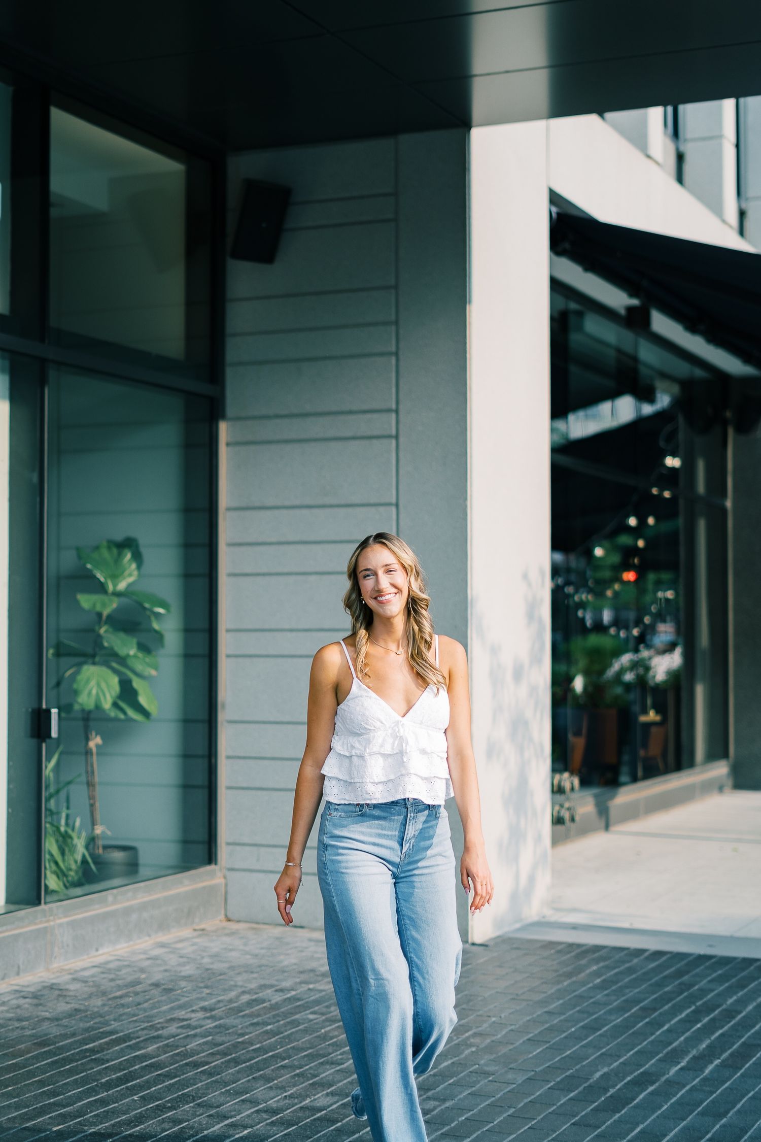 Person in light top and jeans walks through modern building hallway with white columns and natural lighting.
