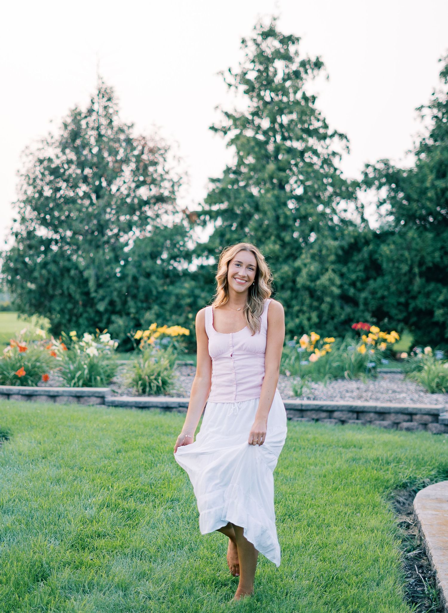 A flowing white dress twirls gracefully in a garden setting with trees and flowers in the background.