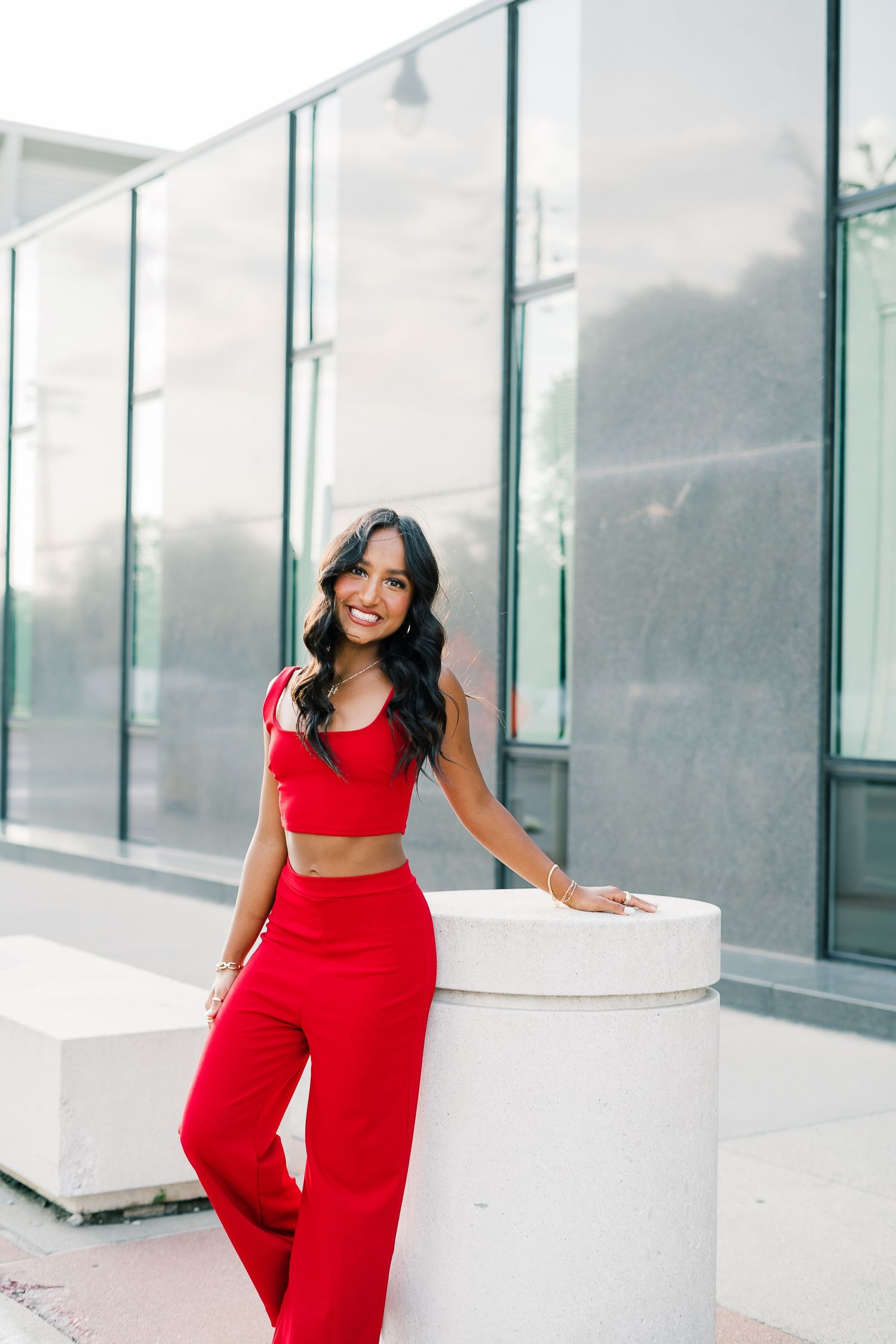 Woman in vibrant red jumpsuit poses confidently against modern white architectural backdrop in lifestyle photoshoot.