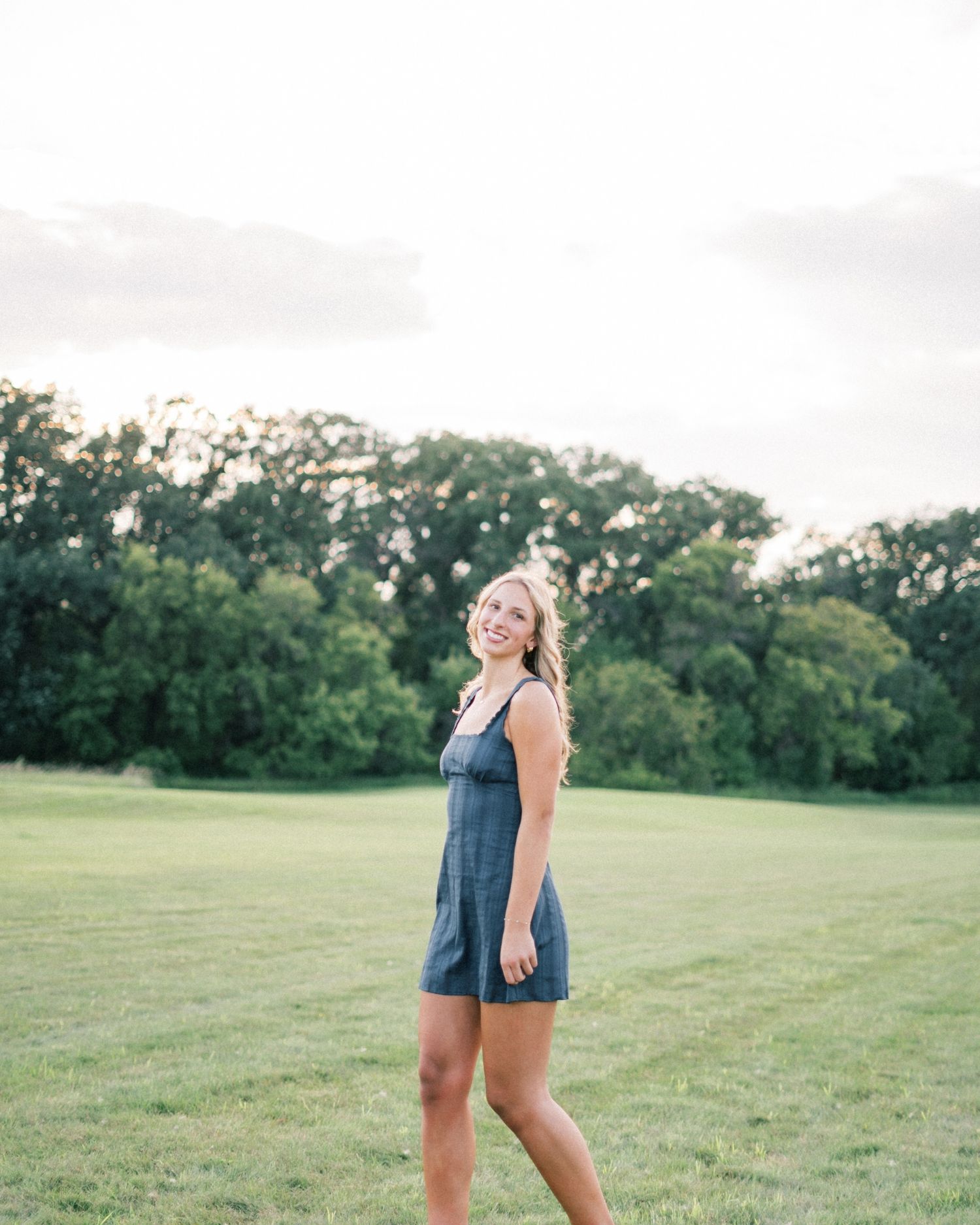 A person wearing denim shorts and a navy blue top walks through a green grassy field at sunset.