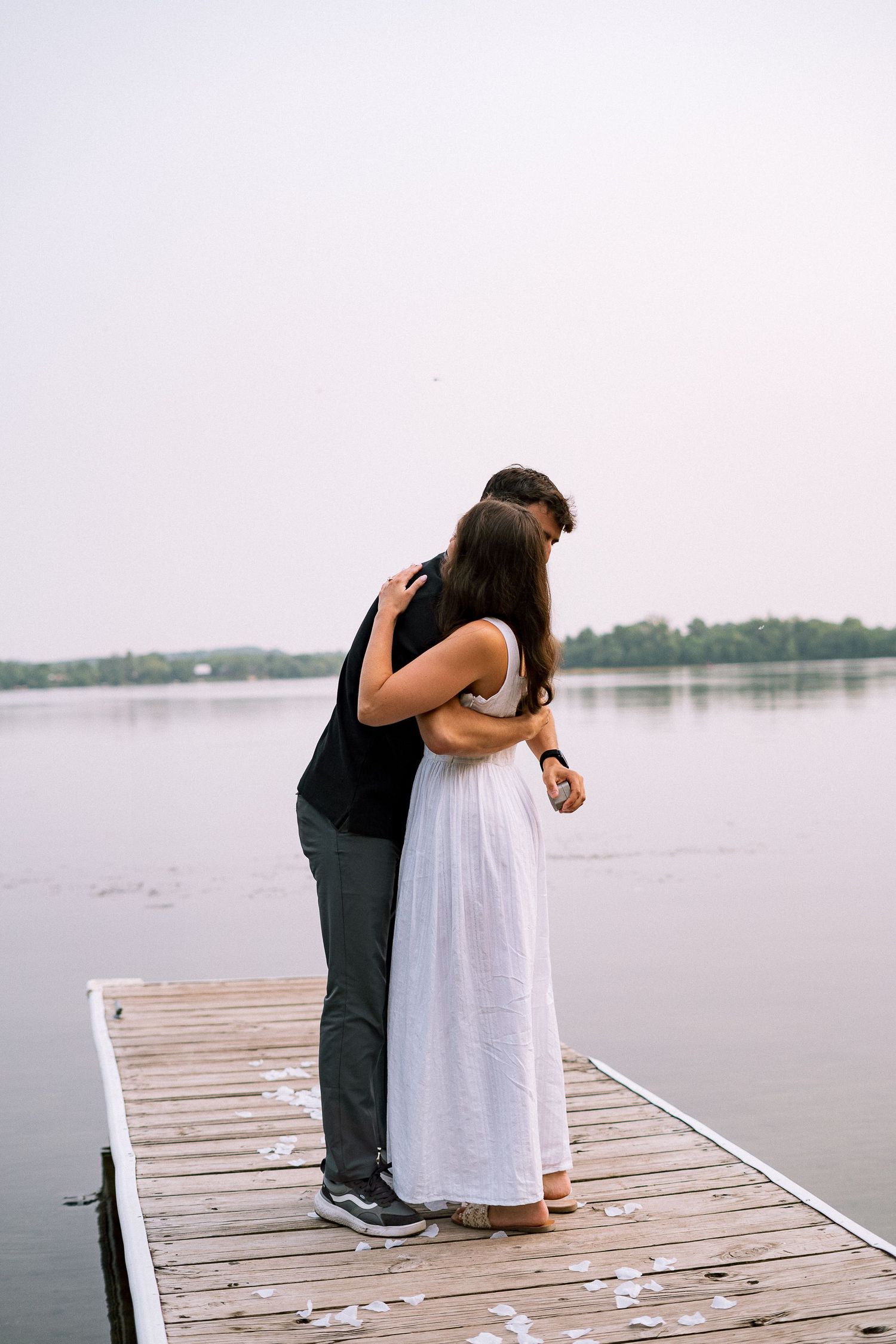 A couple embraces on a wooden dock by a peaceful lake during a special moment.