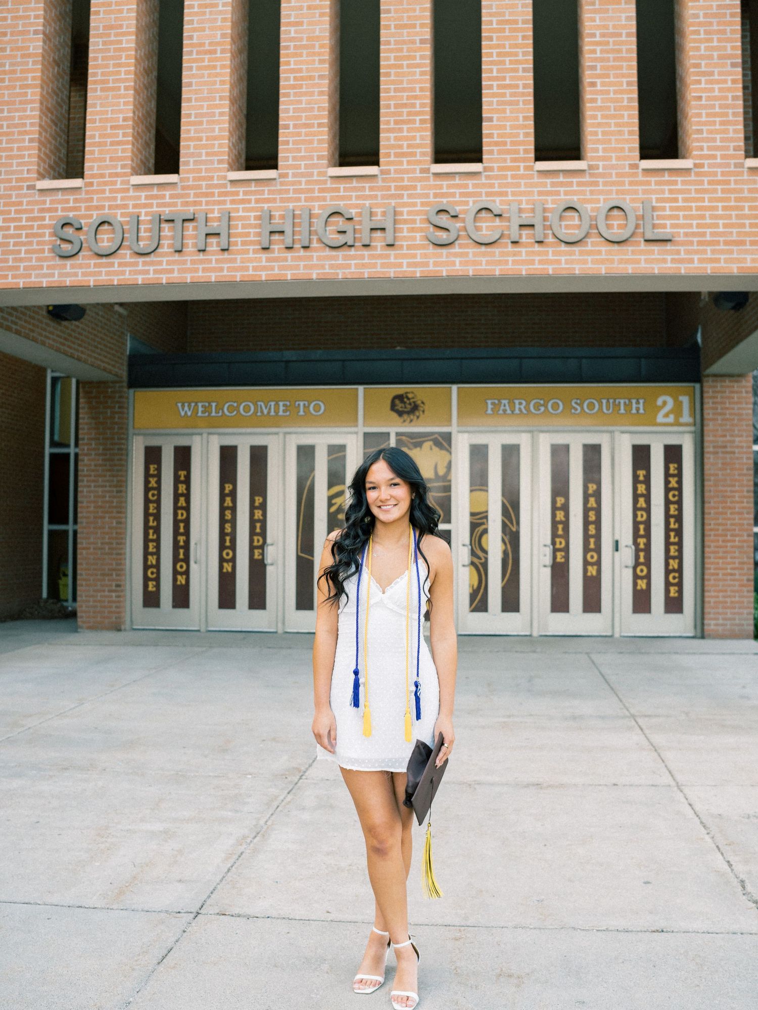 Graduate in white dress poses proudly in front of Largo South High School entrance on graduation day.