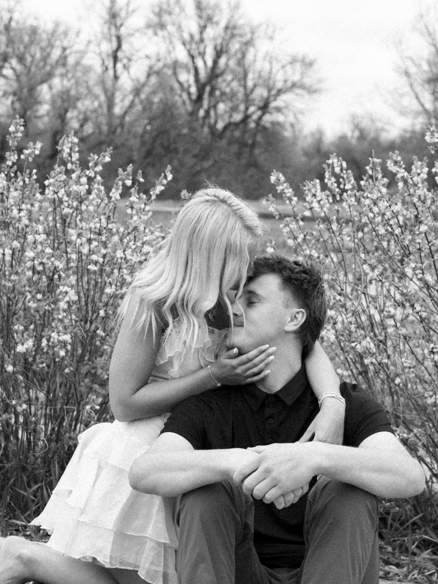 Black and white photo of a couple sharing a tender moment outdoors, surrounded by blooming wildflowers.