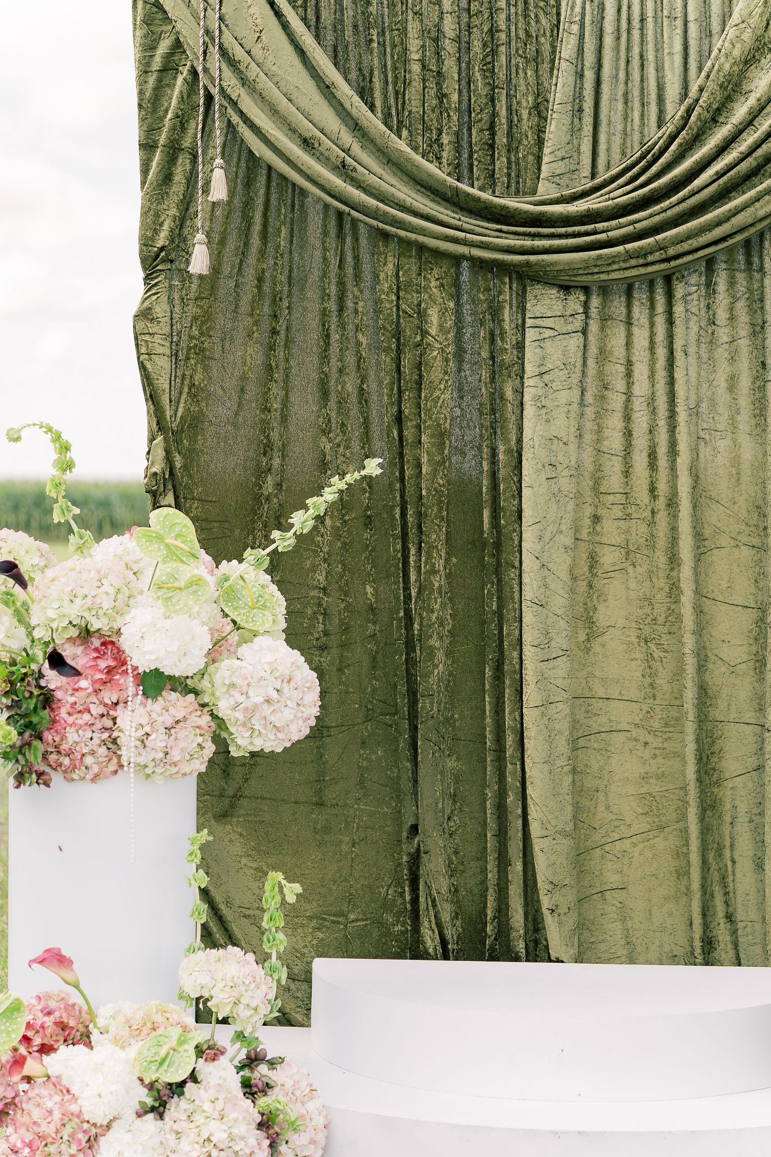 Elegant green velvet drapes with white and pink floral arrangements create an upscale event backdrop.