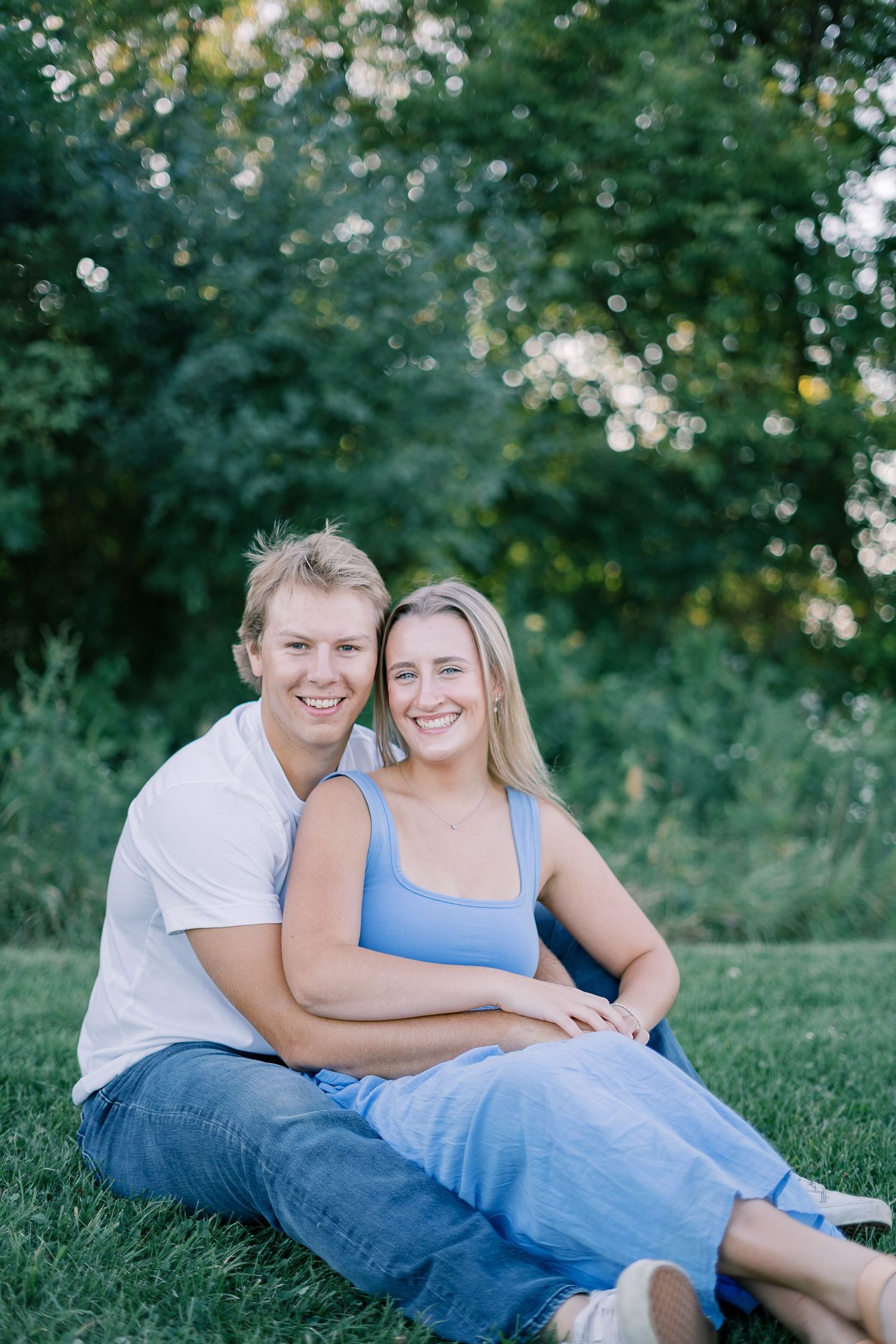 A couple relaxes together on green grass during a sunny outdoor photoshoot.