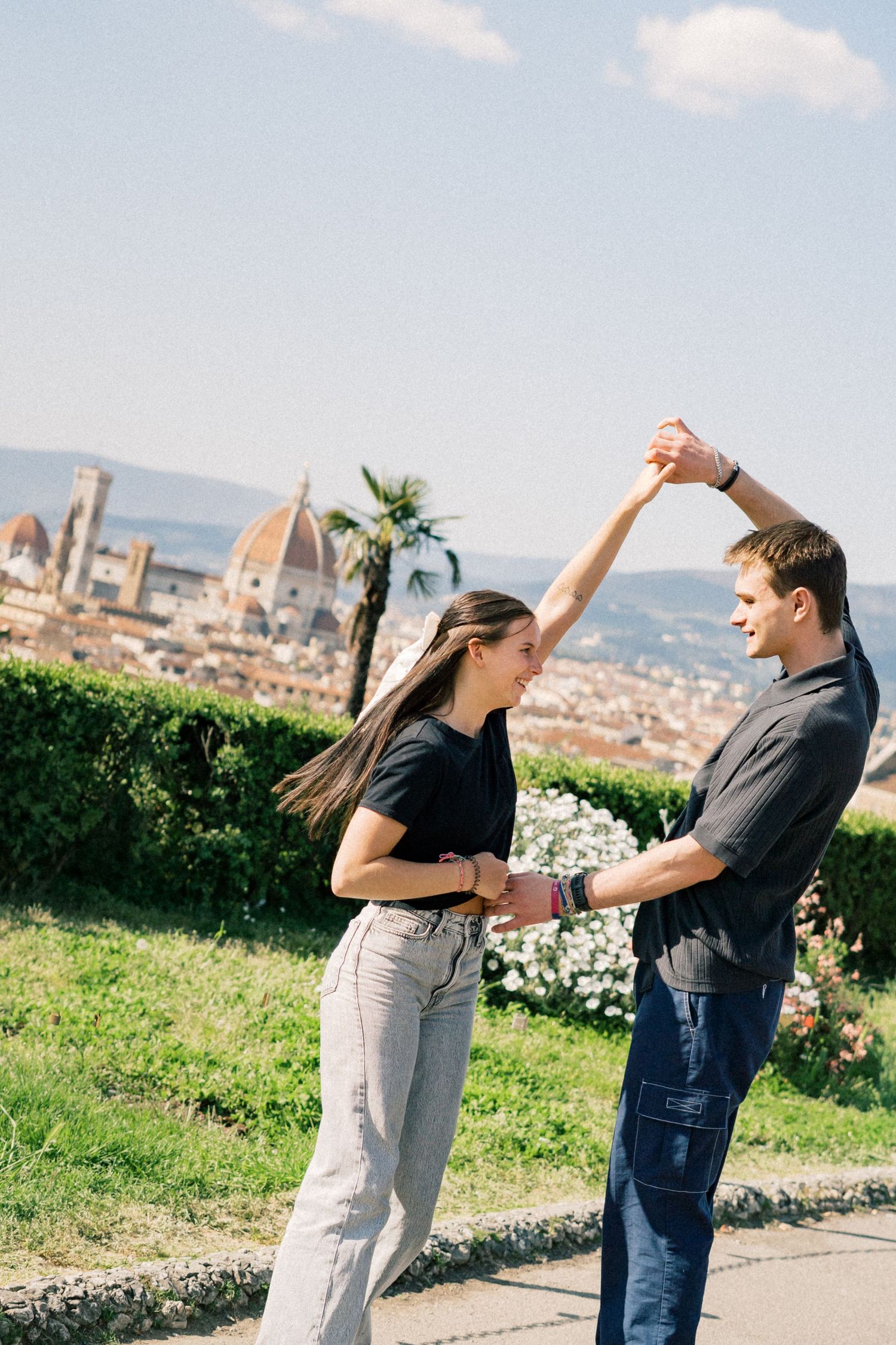 Couple dancing outdoors with Florence cathedral skyline and mountains in background on sunny day.