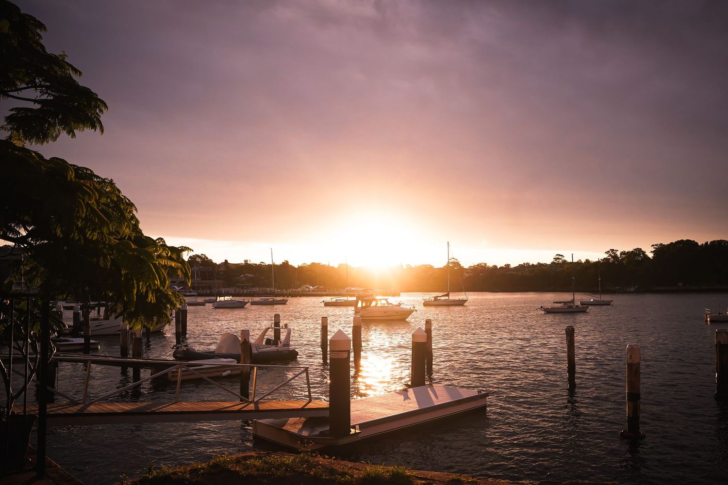 Tranquil sunset over a waterfront dock with boats silhouetted against the glowing sky at dusk.