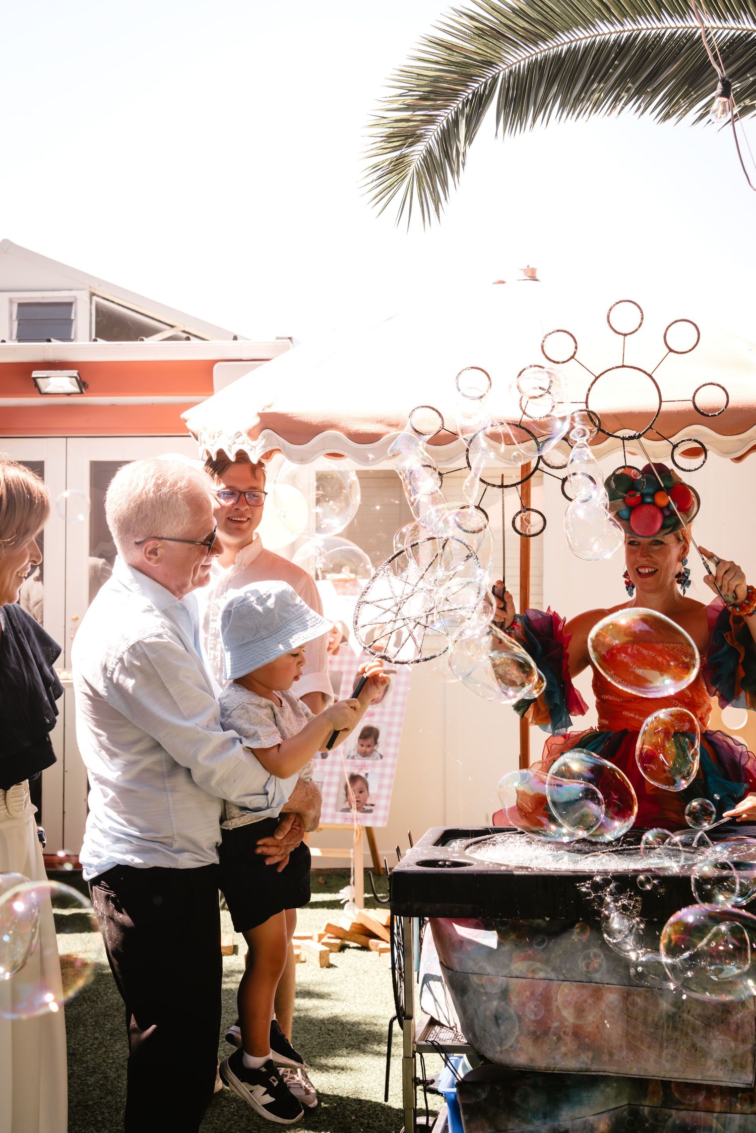 Family enjoying colorful soap bubbles at an outdoor party with a festive bubble performer in bright costume.