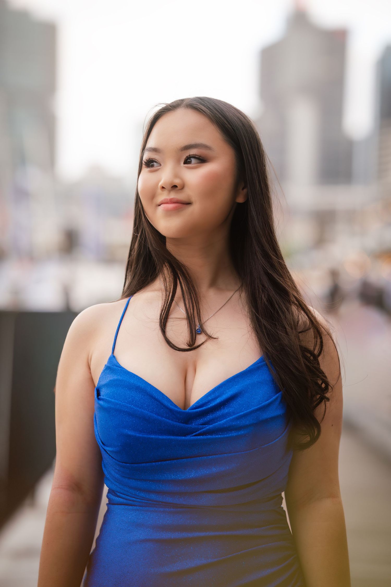 A person in a royal blue satin dress poses outdoors against an urban backdrop.