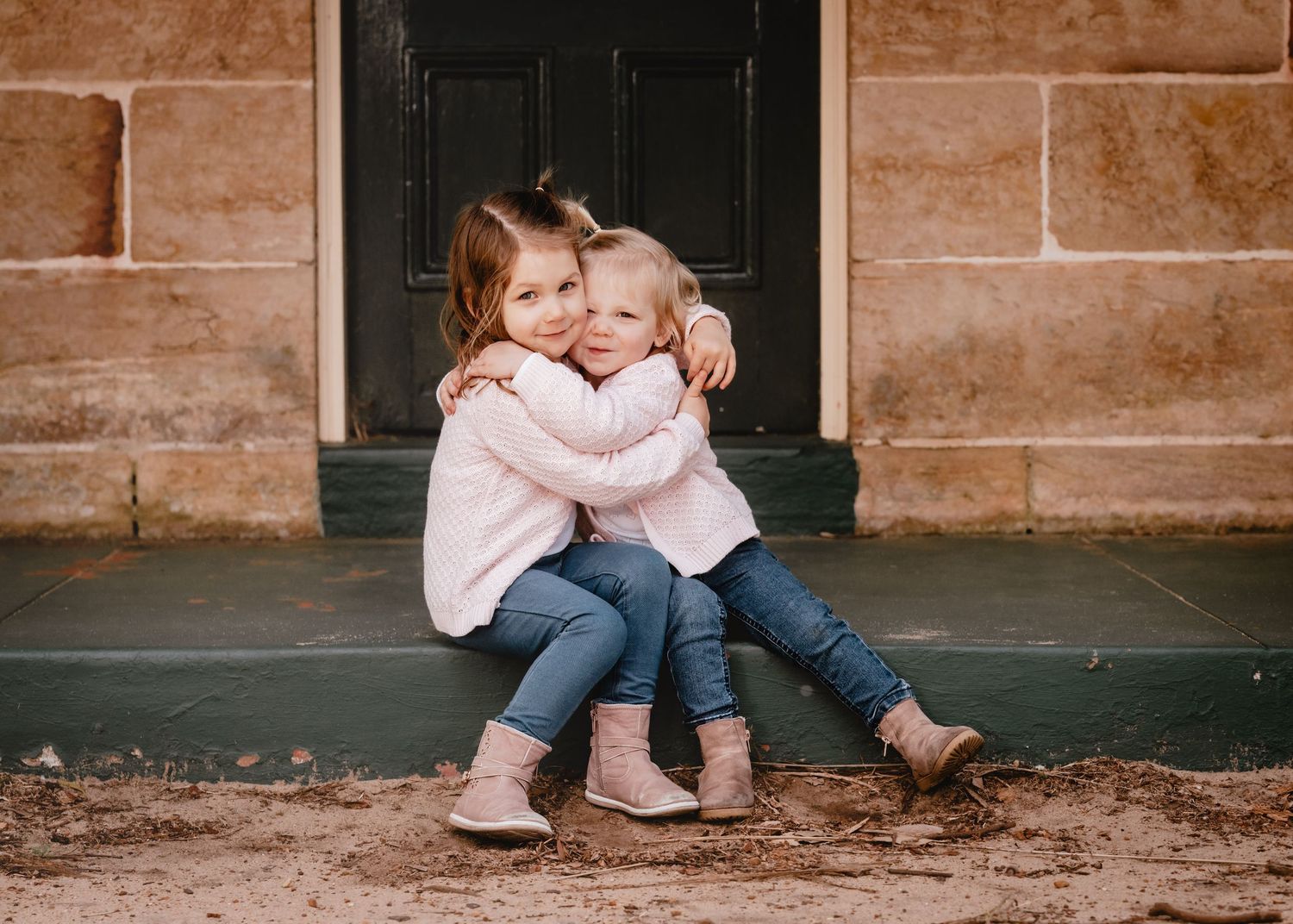Two people sit close together on stone steps in a warm-toned architectural setting.