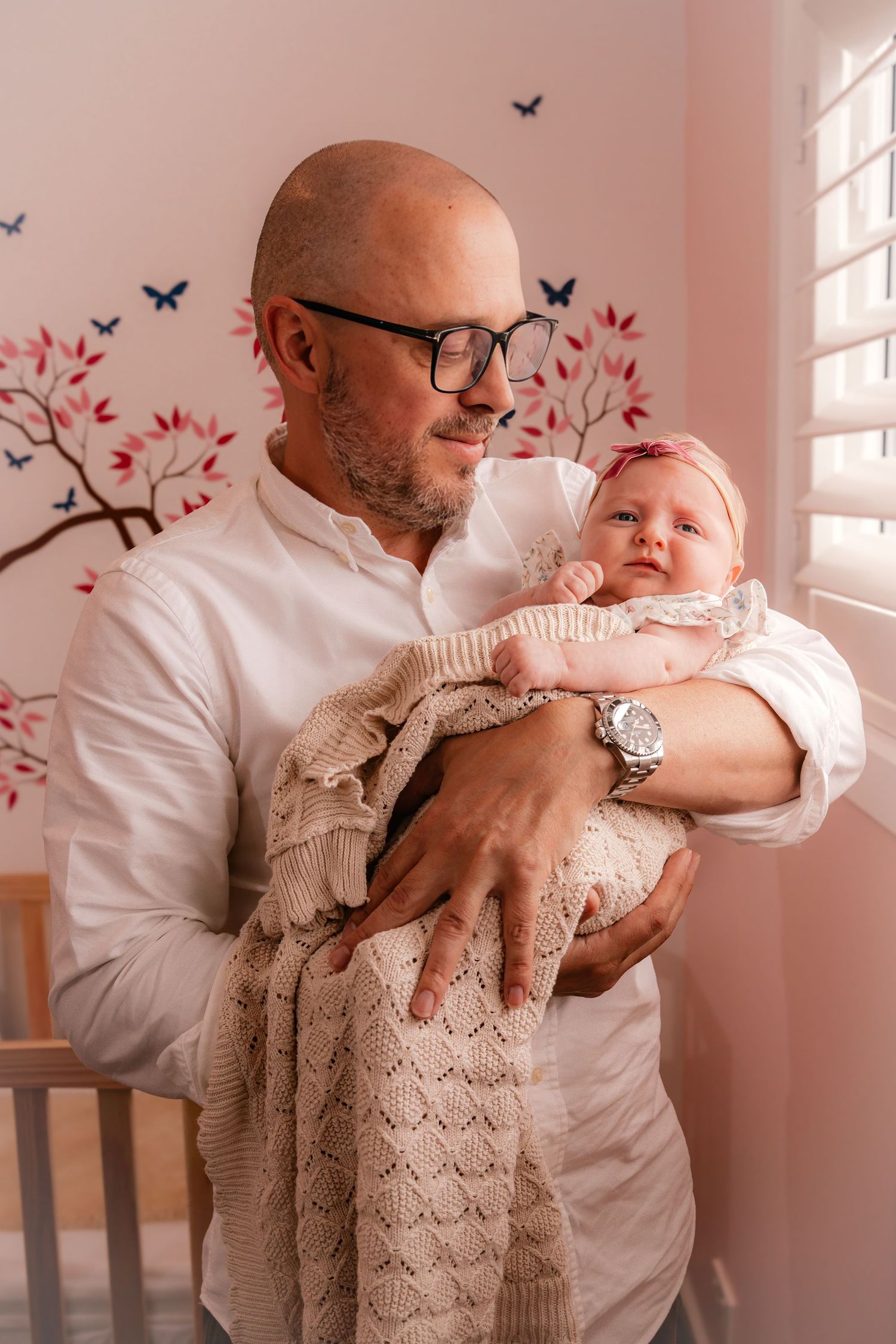 A series of tender moments between a grandfather and baby against a pink wall decorated with butterfly decals.