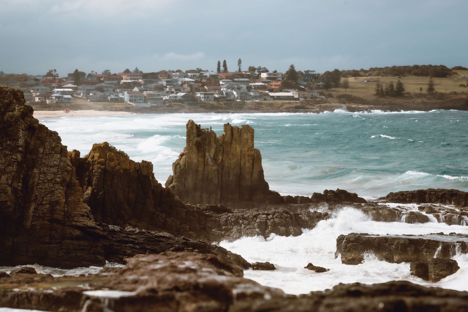 Rocky coastal panorama with rough ocean waves crashing against cliffs under a cloudy sky on a stormy day.