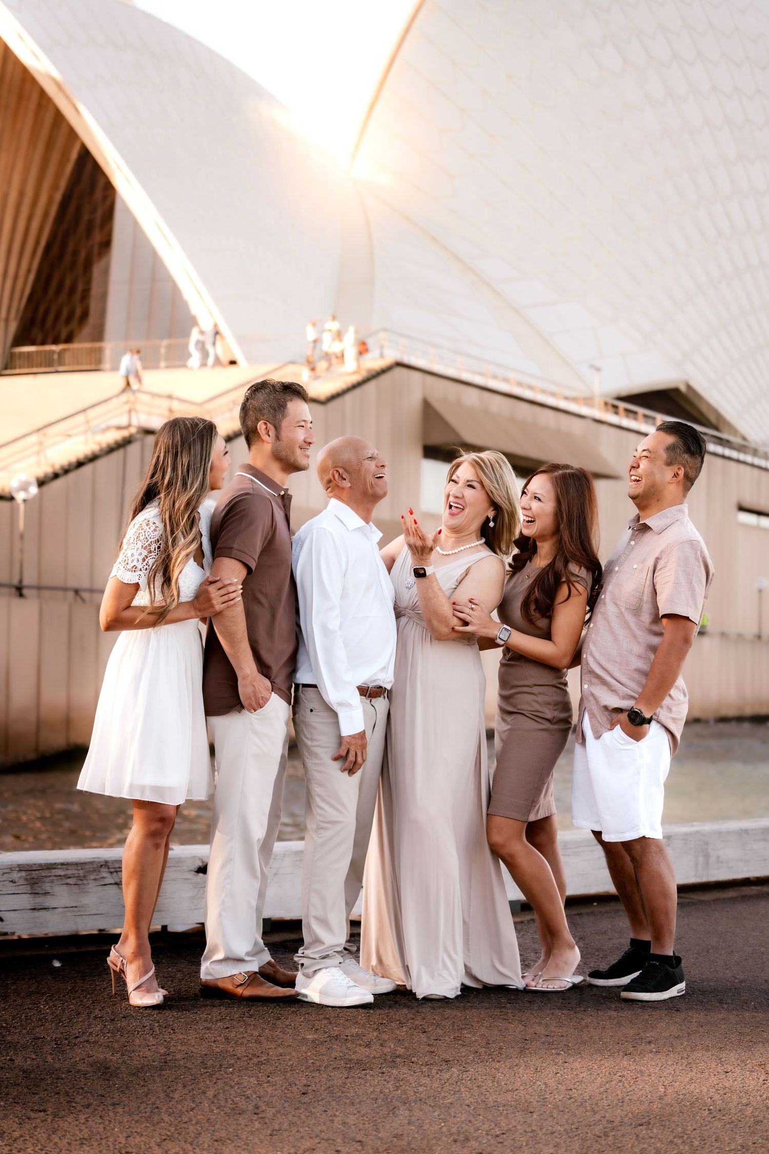 A group of six people in coordinated neutral outfits laughing together outdoors at sunset.