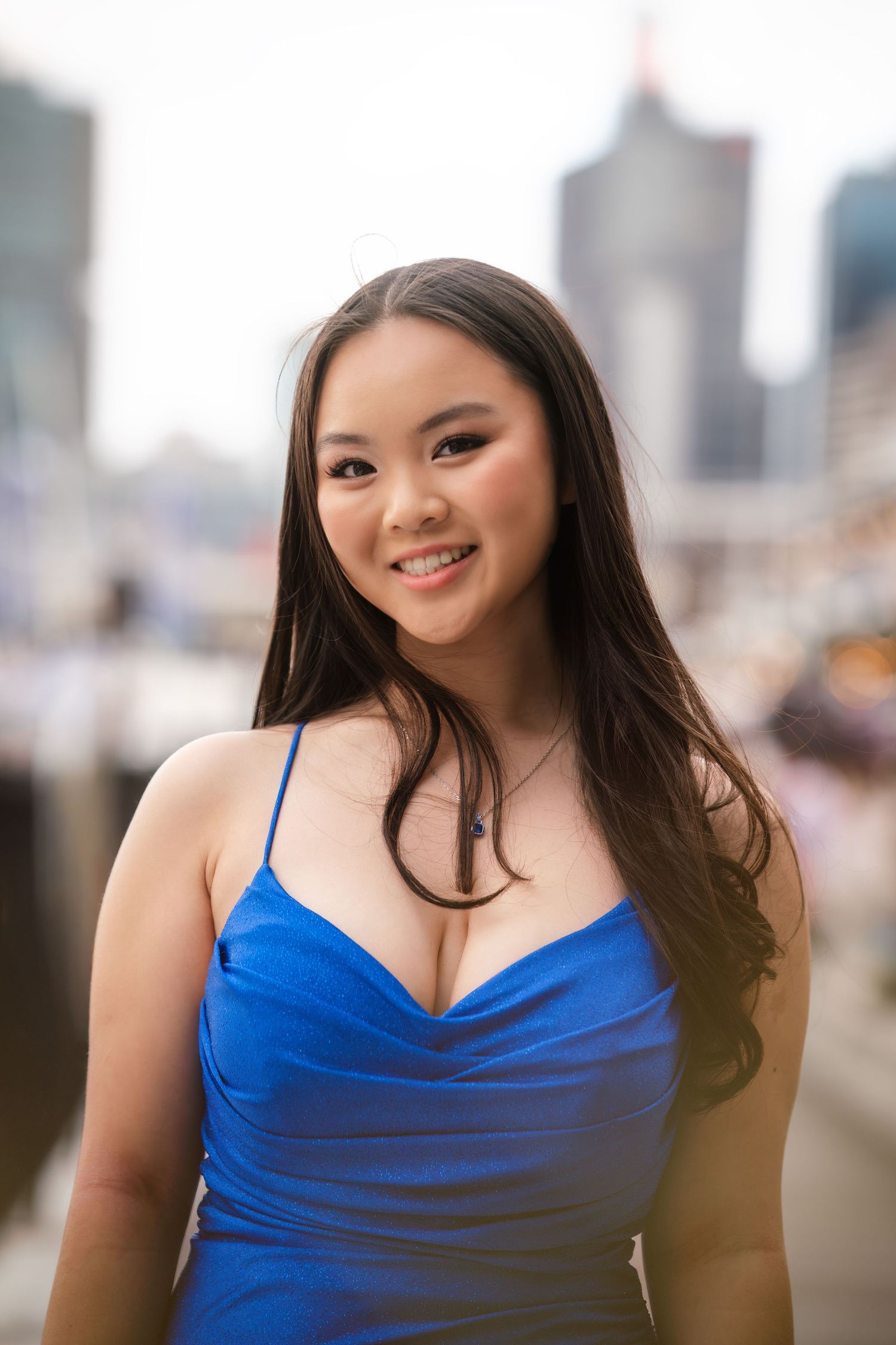 A person in a blue spaghetti strap top poses against an urban cityscape background.